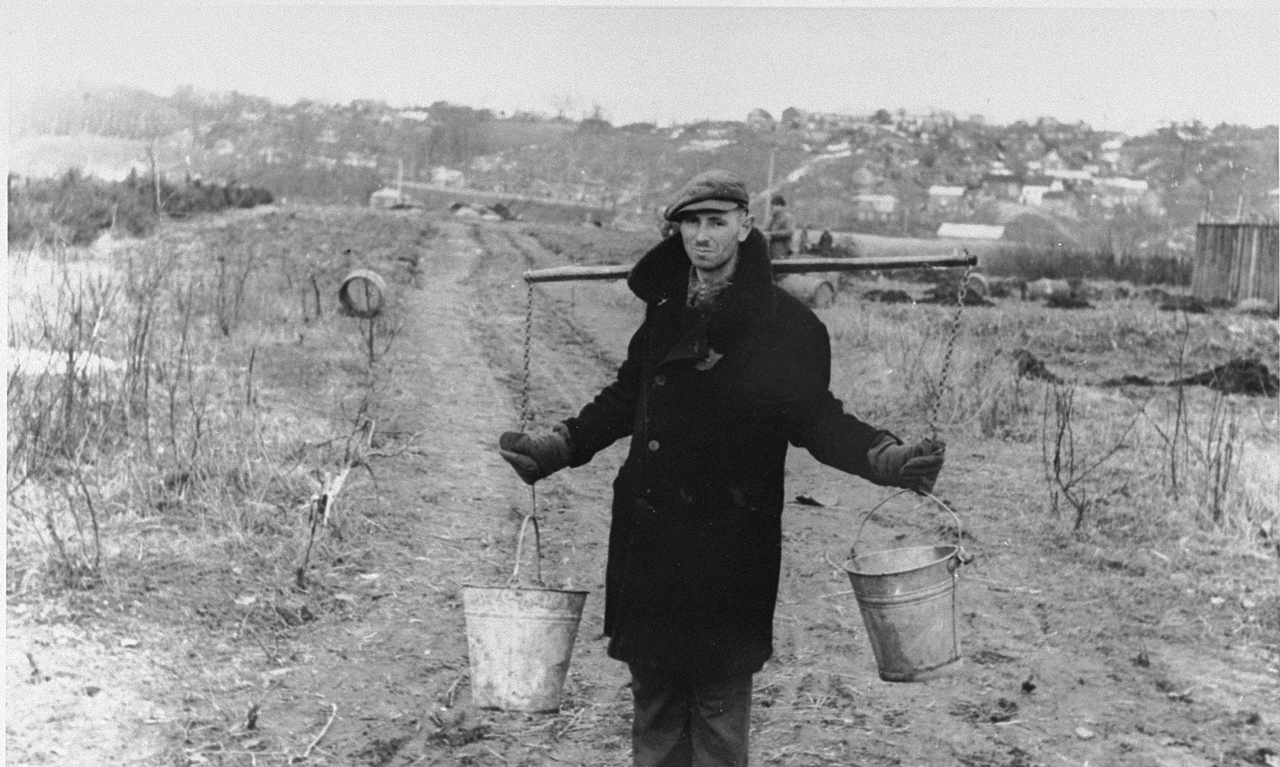 A Jew wearing a yoke across his shoulders carries two pails of water to an agricultural plot in the Kovno ghetto.