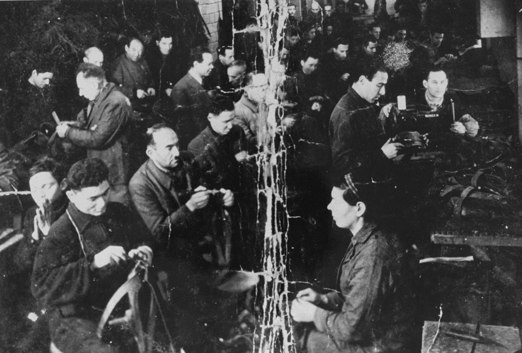 View of Jews at work in the saddle making workshop in the Kovno ghetto.  

Pictured in the center to the left of the crease are Spitulnik and Baruch Grodnik. This photo was kept folded in the pocket of partisan Baruch Gofer while he was living in the forests.