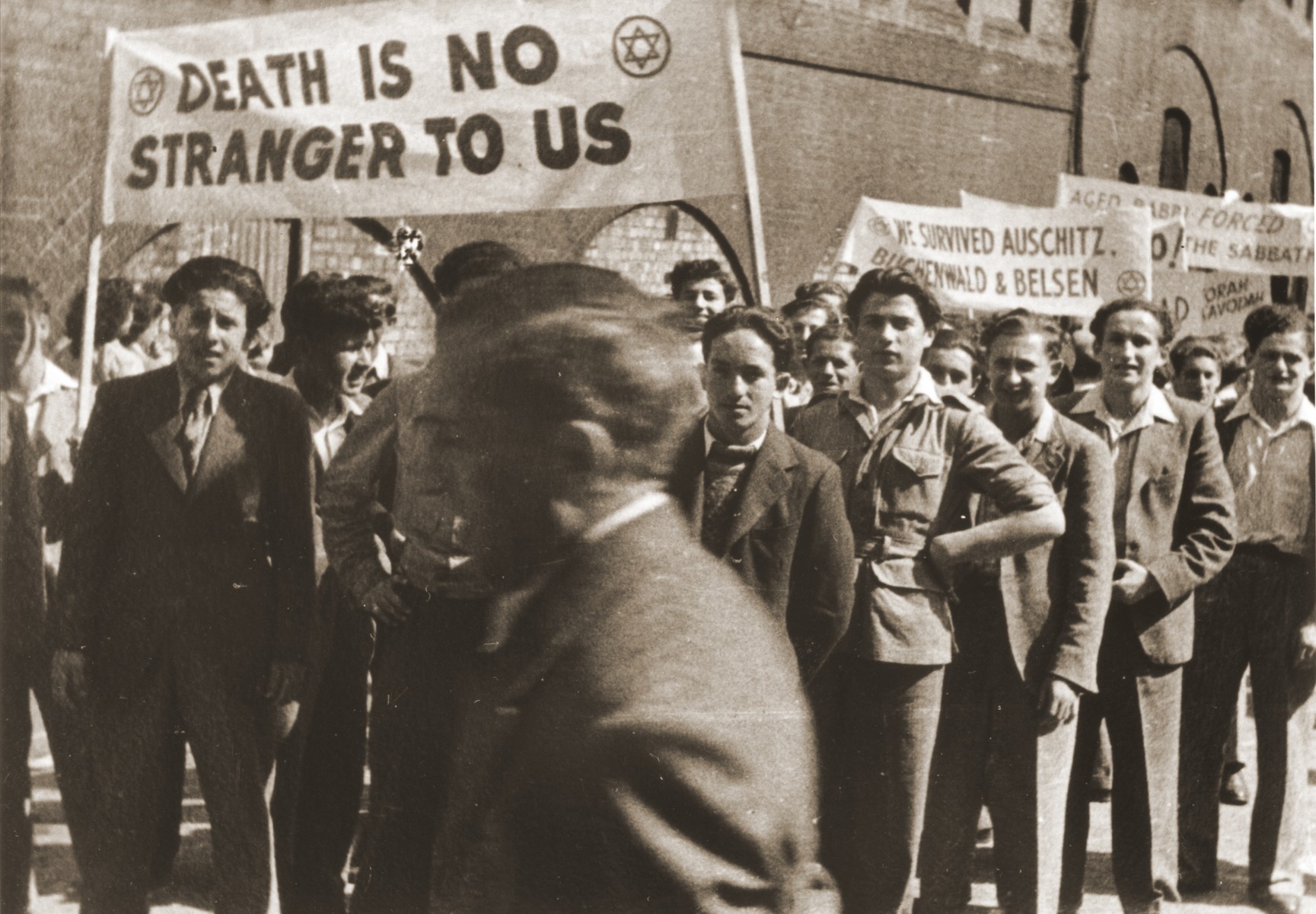 Jewish youth who were brought to England on the orphans transport after the war protest against British policy in Palestine at a demonstration in Trafalgar Square, London.

The young men carry banners that read "Death is no stranger to us" and "We survived Auschwitz, Buchenwald and Belsen".

Moniek Goldberg is on the far right.  Also pictured are Harry Bolsum, Joel Renz and Jonny Fox.