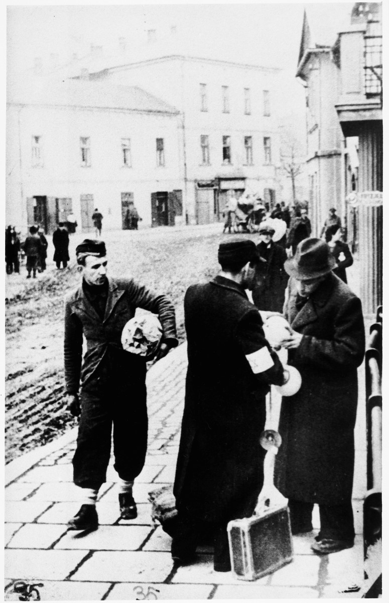 A vendor shows some of his belongings to a fellow Jew on the street of an unidentified ghetto.
