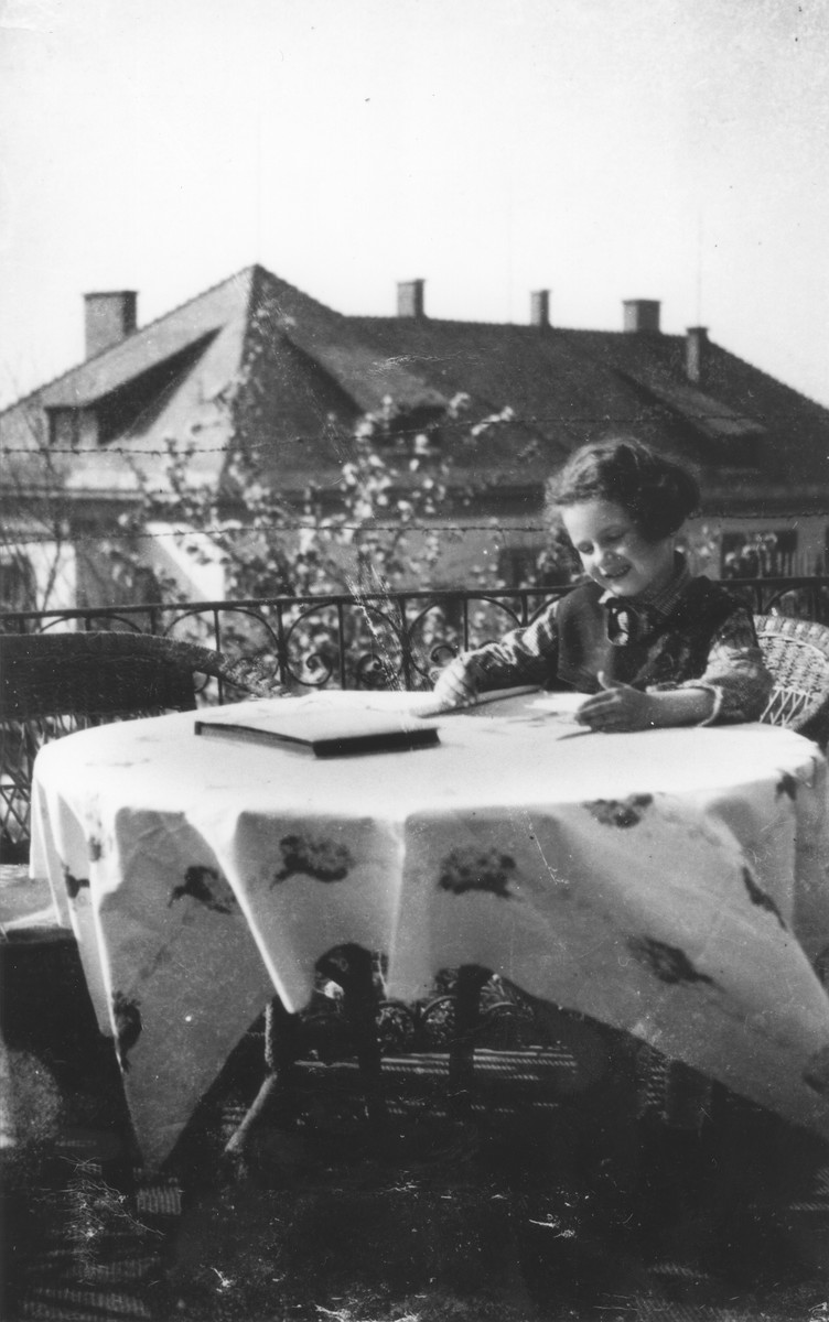 A young Jewish girl sits at a table on the porch of her home.

Pictured is Zuzana Brunnova.