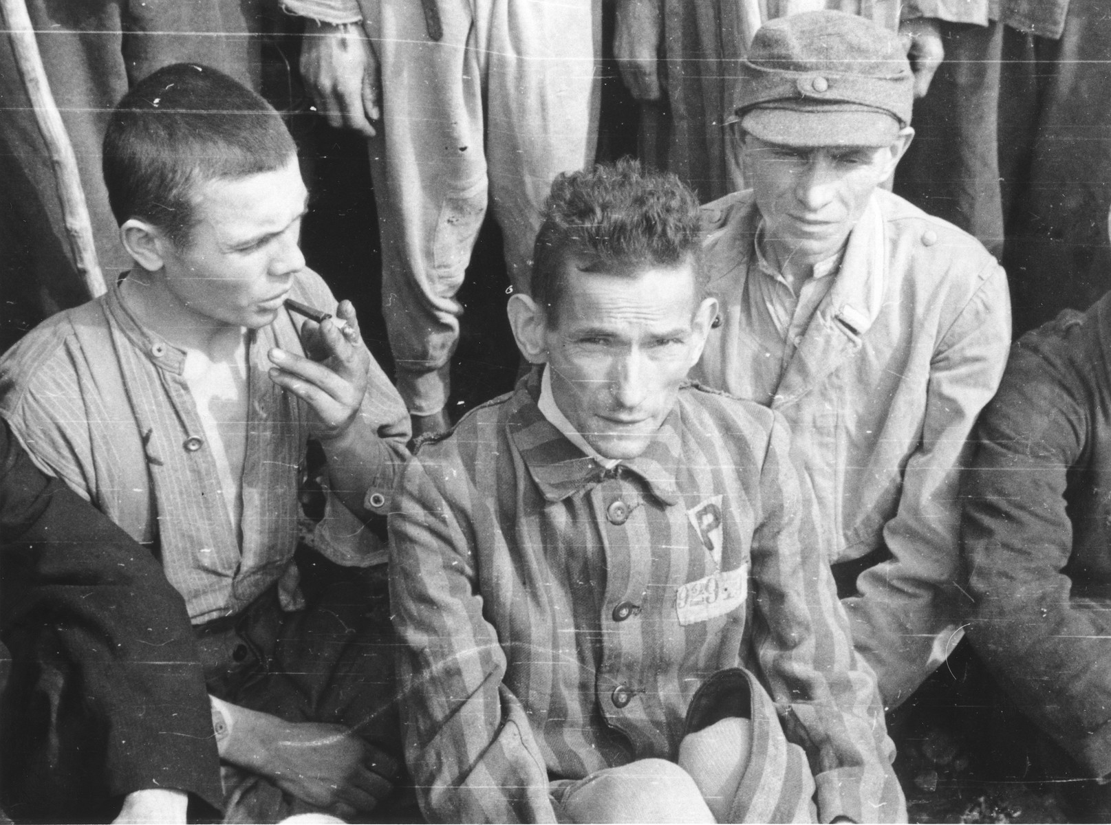 A close-up of three survivors at a gathering in the Langenstein-Zwieberge concentration camp, a sub-camp of Buchenwald, soon after liberation.

The man on the right has been identified as Robert Nardou. The man in the foreground wears a triangular badge with the letter P probably signifying that he was classified as a Polish political prisoner during his incarceration in the camp.