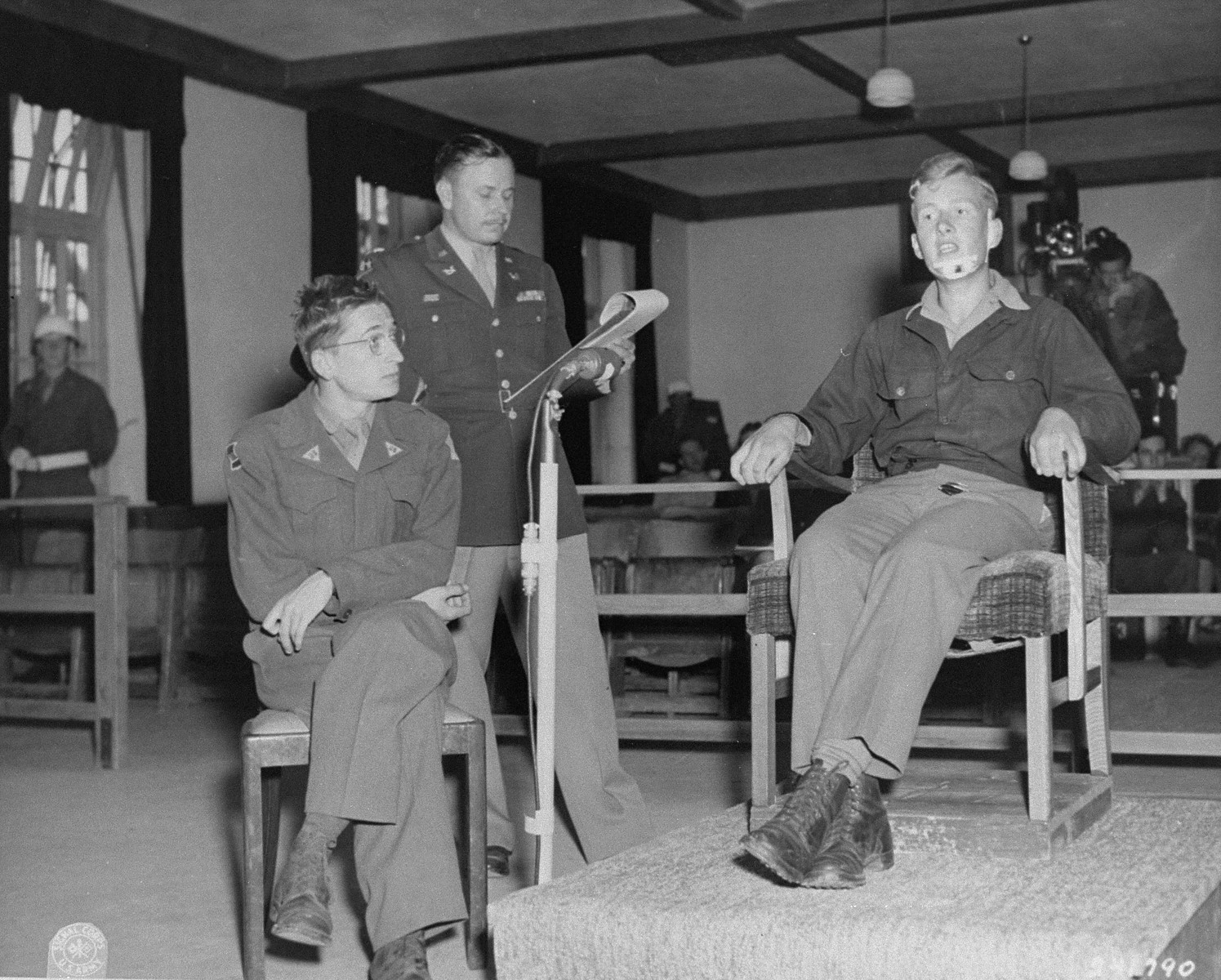 Former SS 2nd Lieutenant Kurt Kramm testifies at the trial of 74 former SS men charged with perpetrating the Malmedy atrocity. 

Pictured from left to right are: Herbert Rosenstock, an interpreter; Lt. Col. Burton F. Ellis; and Kramm.