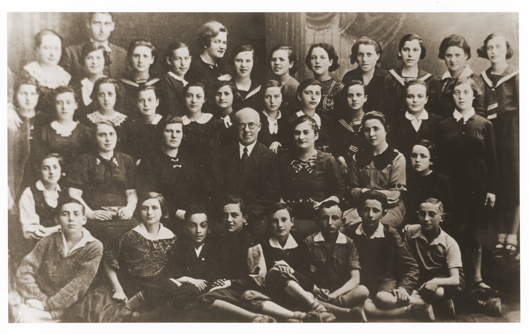 Class portrait of students at the Jewish public school in Mlawa, Poland.  

Gittel Blankitner is seated in the second row from the front on the far right.

Gerzon Trzcina was born in Krasnosielc, Poland in 1922.  He was the son of Dina Kassel and Benam Yitzhak, who was a businessman in the leather trade.  Gerzon had one older brother, Jacob, and two sisters, Faiga (b. 1918) and Perl (b. 1920).  When the war broke out, Gerzon was working as a photographer's assistant (among other jobs) in Warsaw.  Following the German invasion of September, 1939, Gerzon was slightly wounded by shrapnel.  Soon after, a drunken German soldier, forcibly cut Gerzon's hair.  When the soldier made him stoop down to pick up the cuttings, Gerzon grabbed the German's gun and ran away.  After a short time in hiding, Gerzon returned to his hometown, where he learned that eighty Jews had been murdered in the synagogue during the first week of the war in one of the first large-scale atrocities against Polish Jews.  Among those killed was Gerzon's eighty-two-year-old grandfather, Haskel Kassel.  Gerzon moved on to Makow Mazowiecki, where he was forced to clean the stables the Germans had set up in the town's synagogue.  In the late fall, Gerzon escaped with his family to Bialystok, where he worked in a tannery until the family was deported to the Soviet interior in June, 1940.  Along with a group of Polish and Jewish refugees, the Trzcinas were sent to the Kiltovo labor camp in northern Russia.  Harsh conditions and poor nutrition led to Gerzon's father's death in the camp.  The family remained in Kiltovo until the German invasion of the Soviet Union in June of 1941.  Soon after, the refugees were allowed to leave the camp, and the Trzcinas moved to nearby Syktyvkar (capital of the Komi republic), where Gerzon worked in a construction company and later in a tannery.  In Syktyvkar, Gerzon was reunited with Gittel Blankitner, a Jewish refugee from Mlawa, whom he had met earlier in his travels in the Soviet Union.  (Gittel's father perished in Aushwitz, and her mother and siblings were killed in Treblinka.) In November, 1944, Gerzon and Gittel were married. The couple left the Soviet Union with their new baby in 1946.  Returning for a brief time to Poland, the family soon joined the wave of survivors streaming toward the Western zones of occupation.  After their arrival in Germany, the Trzcinas stayed in several DP camps including Vilseck, Wurzburg and Lechfeld, where Gerzon worked as an UNRRA photographer.  In March 1951, the family immigrated to the United States.