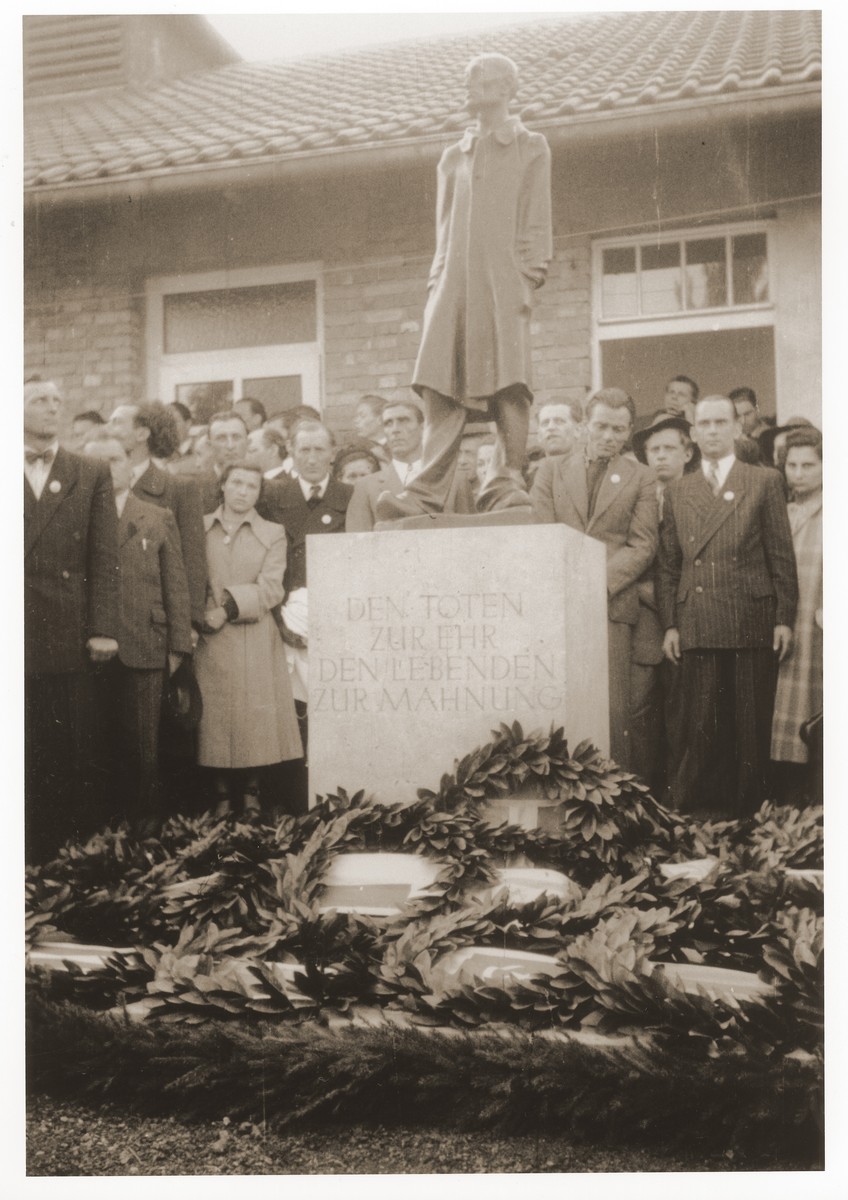 Jewish DPs gather around a memorial sculpture at the Dachau concentration camp.  

The inscription on the pedestal reads, "To honor the dead and admonish the living".  At the base of the memorial are wreaths brought by delegations from a host of foreign countries.