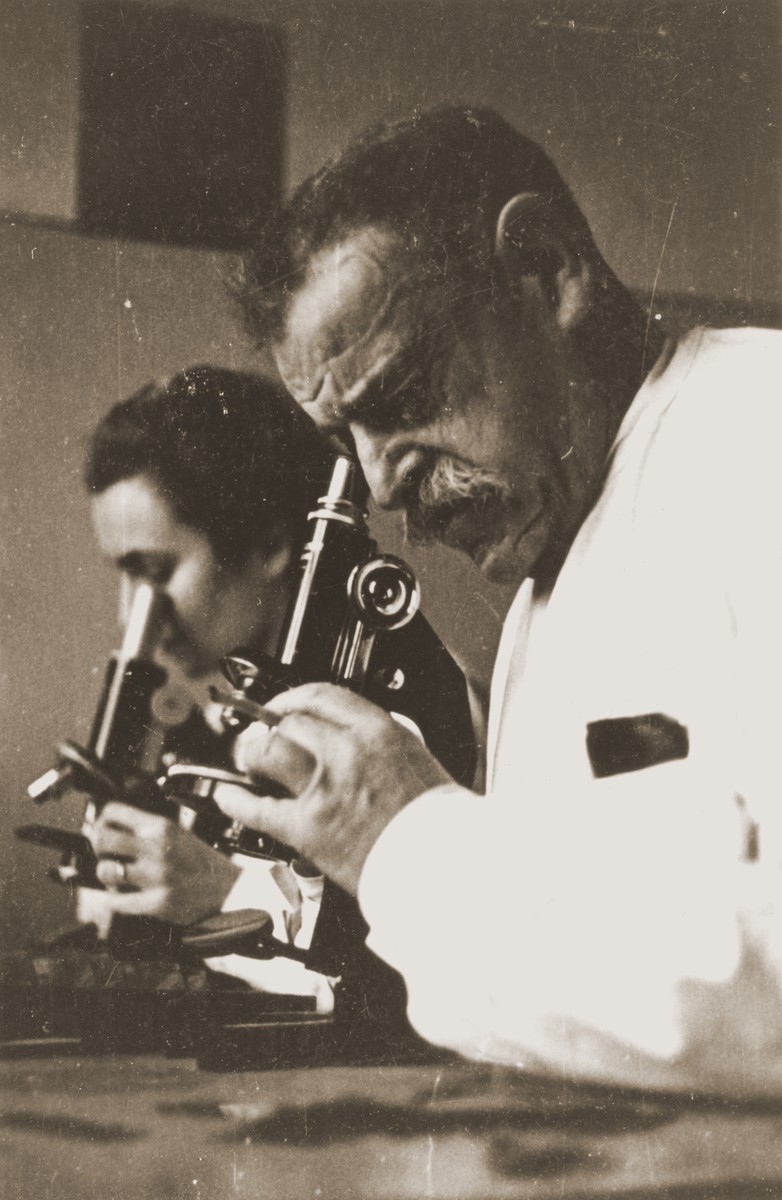 Professor Wilhelm Caspari and a female assistant conduct medical research using microscopes in the laboratory of the main hospital in the Lodz ghetto.

Wilhelm Caspari (1872-1944), was born in Berlin.  He originally studied clinical medicine and became a general practitioner.  In the course of his practice, he turned to bacteriological studies, published a series of scholarly papers, and habilitated as a docent at the University of Berlin.  Cancer research became his area of specialization.  On the basis of his scientific findings, Caspari was offered a chair at the Speyer clinic in Frankfurt am Main, where he worked until the summer of 1933.  He came to the Lodz ghetto in October 1941 with the Frankfurt transport.  Rumkowski immediately accorded him special status, enabling Caspari to continue his research at the main hospital on Lagiewnicka Street.  He was assigned a residence at the rest home in Marysin.  From February, 1942 until December, 1943, Caspari gave talks about nutritional conditions in the ghetto.  After the main hospital was shut down, Caspari was moved to the Department of Vital Statistics, where he compiled tables relating to the mortality rate, and to the caloric and vitamin content of the ghetto diet.  Caspari's wife was deported in September, 1942.  He remained in the ghetto, but his health soon deteriorated.  He contracted influenza during the epidemic of 1943 and succumbed to pneumonia on January 21, 1944.  [L. Dobroszycki, The Chronicle of the Lodz Ghetto 1941-1944, pp.435-6]