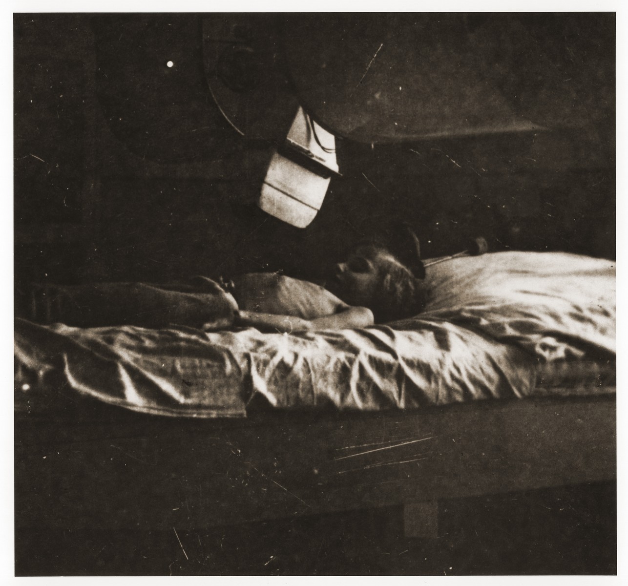 An emaciated young child lies in a bunk in the Lodz ghetto.