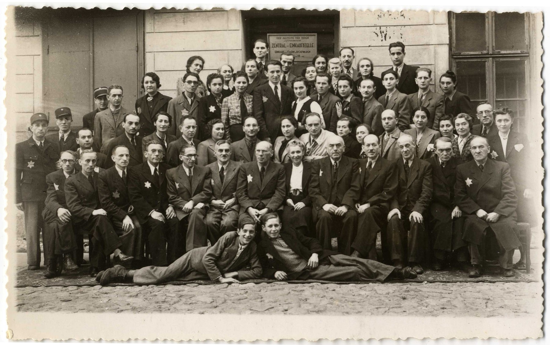 Group portrait of the employees of the Zentral Einkaufstelle, the central purchasing department of the ghetto which provided raw materials to the other ghetto workshops.

Pictured in the front row, sixth from the left is Gustaw Gerson, the director of the Einkaufstelle.  To his immediate right and in the center of the photograph is Dawid Warszawski, head of the textile workshops.