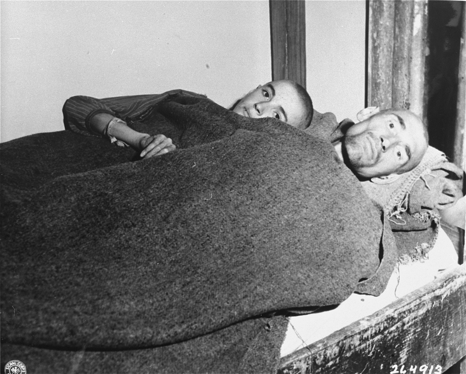 Two emaciated survivors lie in a single bed in the newly liberated Gusen concentration camp.