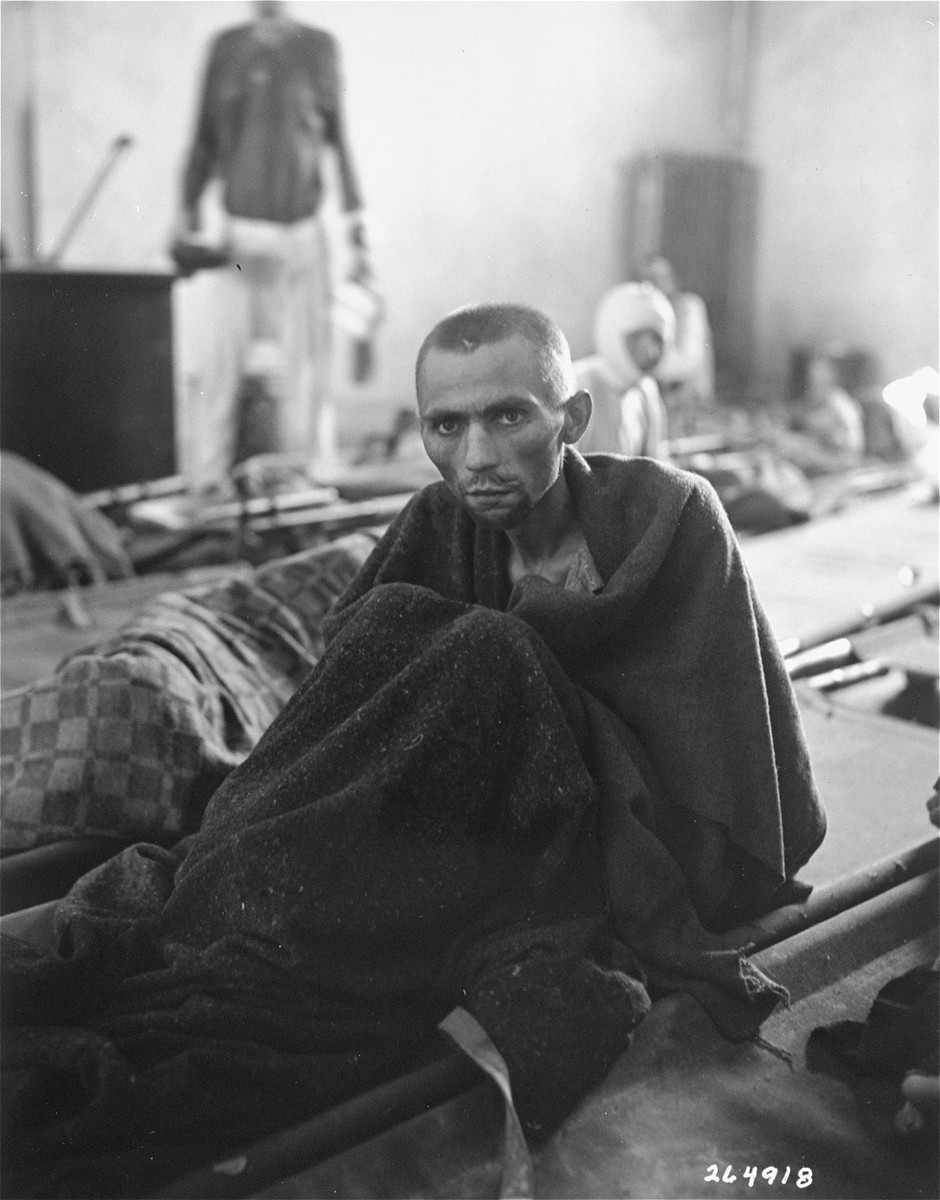 An emaciated survivor wrapped in a blanket sits up on a stretcher in the newly liberated Gusen concentration camp.