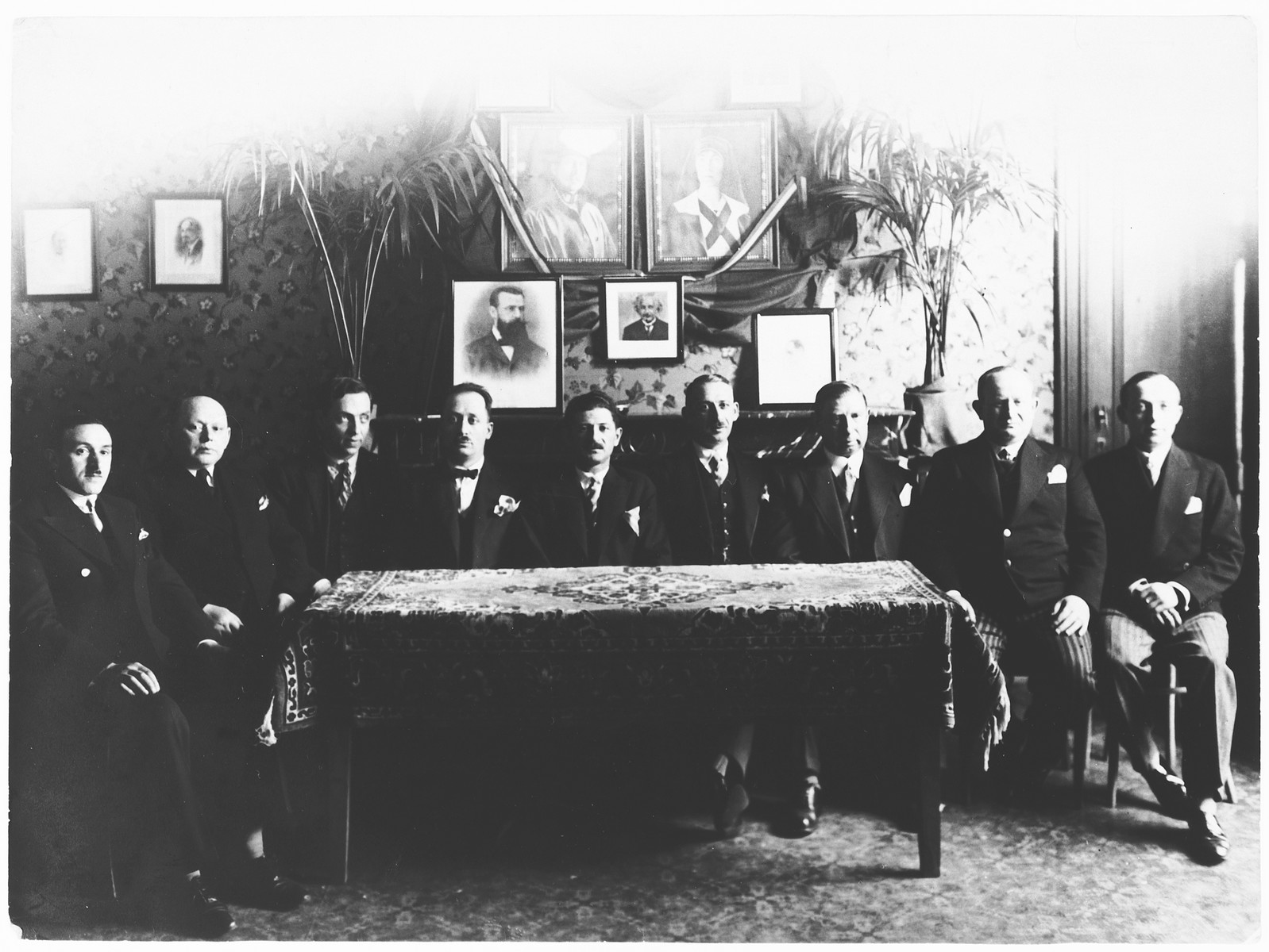 Group portrait of members of the ftraternal organizatgion of Jews from Lodz  in Antwerp, Belgium.

Among thos pictured is Emmanuel Rubinstein, on far left.  Hanging on the wall are portraits of the King and Queen, Theodore Herzl and Albert Einstein.