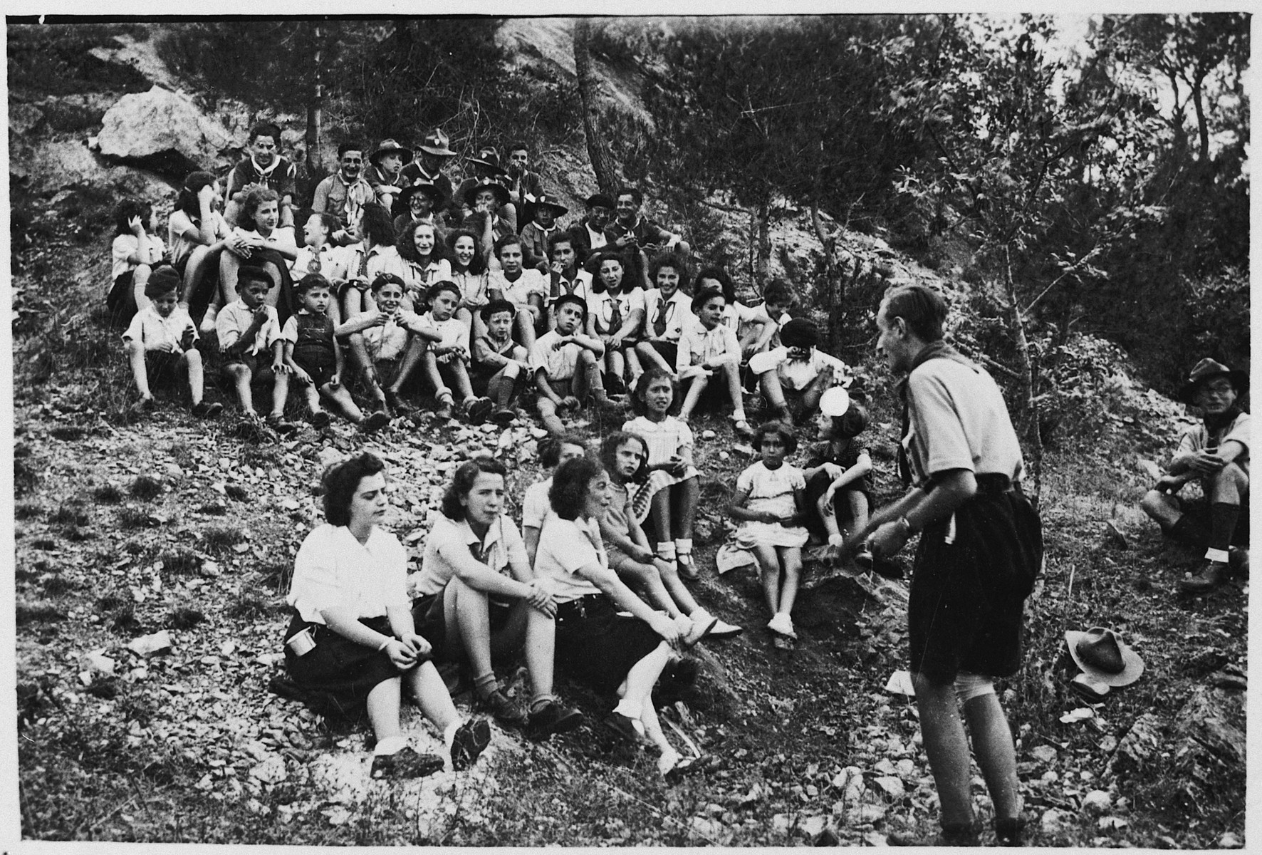 Robert Gamzon (Castor) addresses a group of the Eclaireurs Israelites de France (Jewish Scouts) who are seated on a hillside.