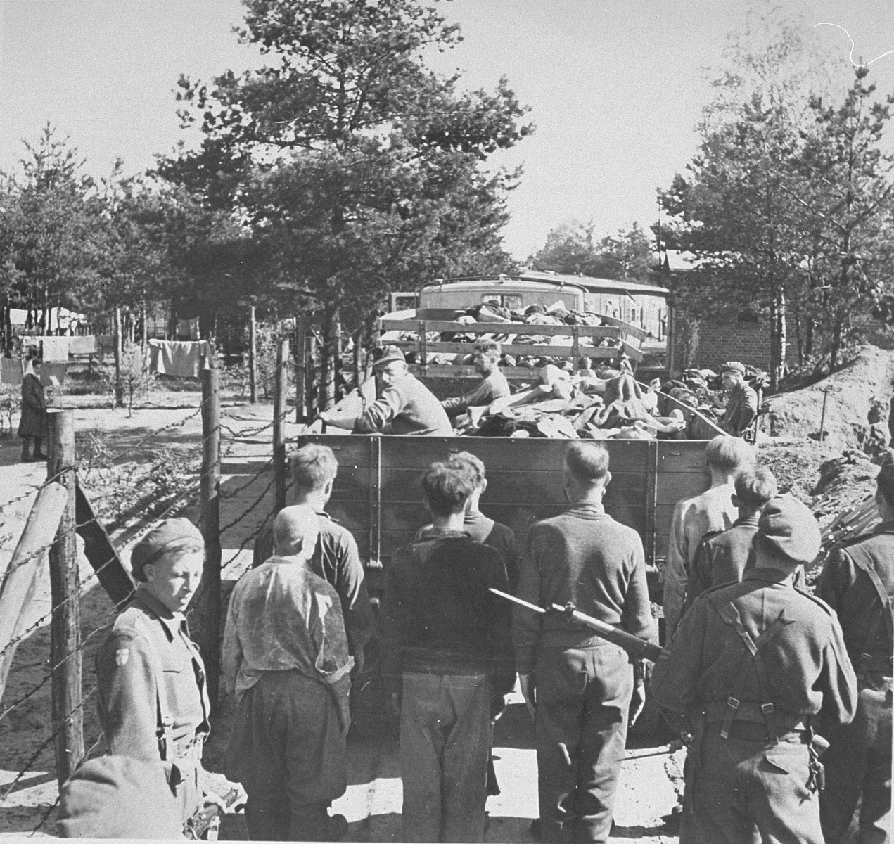 British soldiers transport former SS guards and truckloads of corpses to mass graves for burial.  

Former camp doctor Fritz Klein can be seen seated in the back of the lorry.