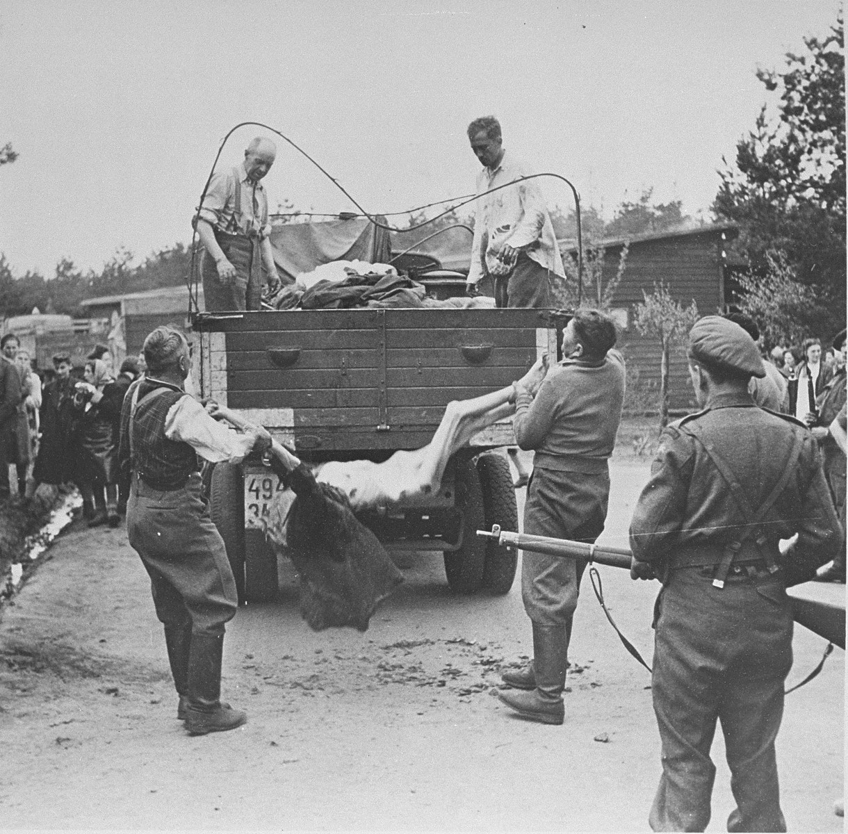 SS guards are forced to load corpses onto a truck while under the supervision of British soldiers.

Original caption reads:  "S.S. men captured at the camp, are made to load lorries with bodies to be taken away for burial."
