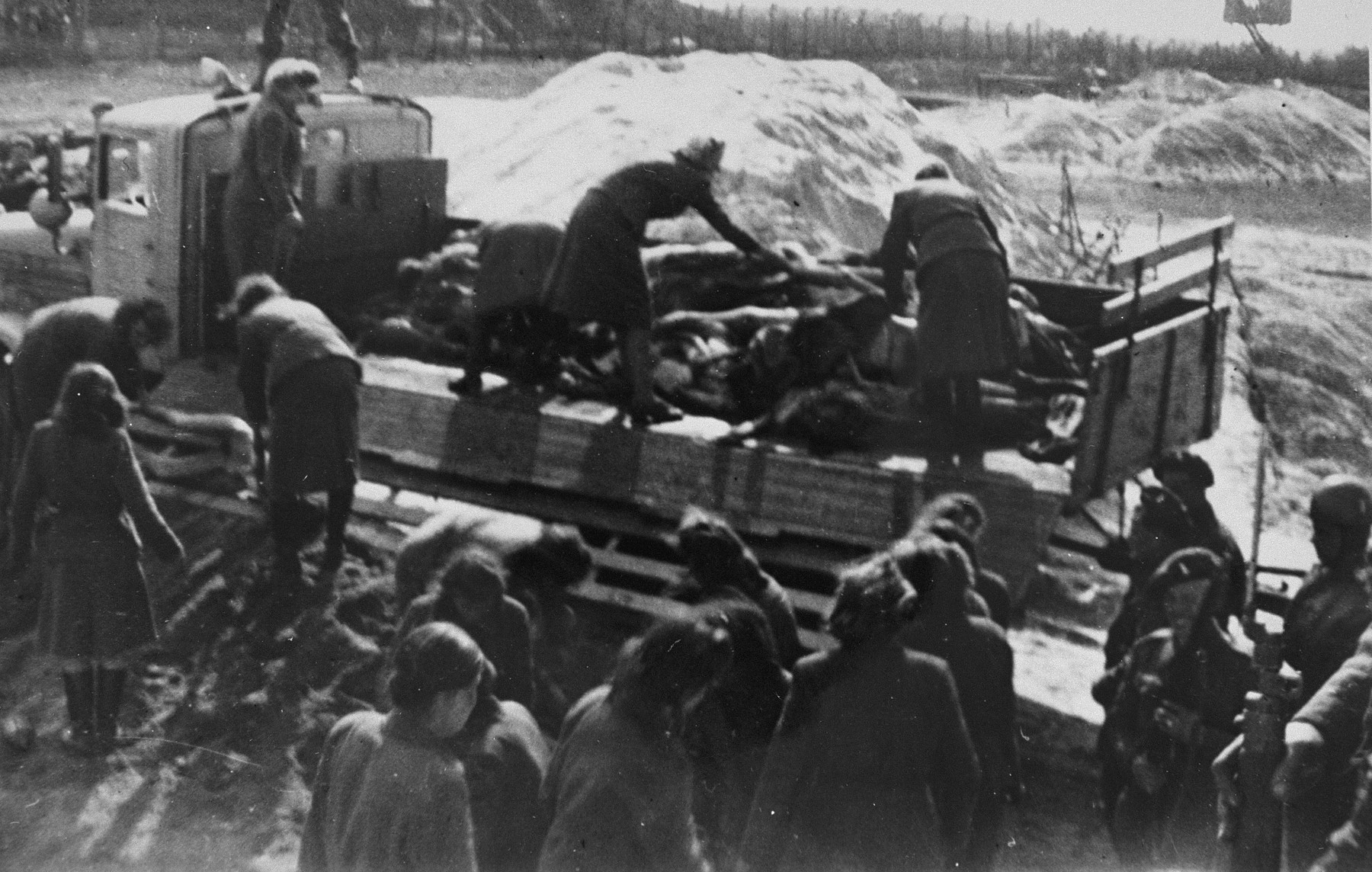 Former camp personnel unload a truckload of corpses into a mass grave.