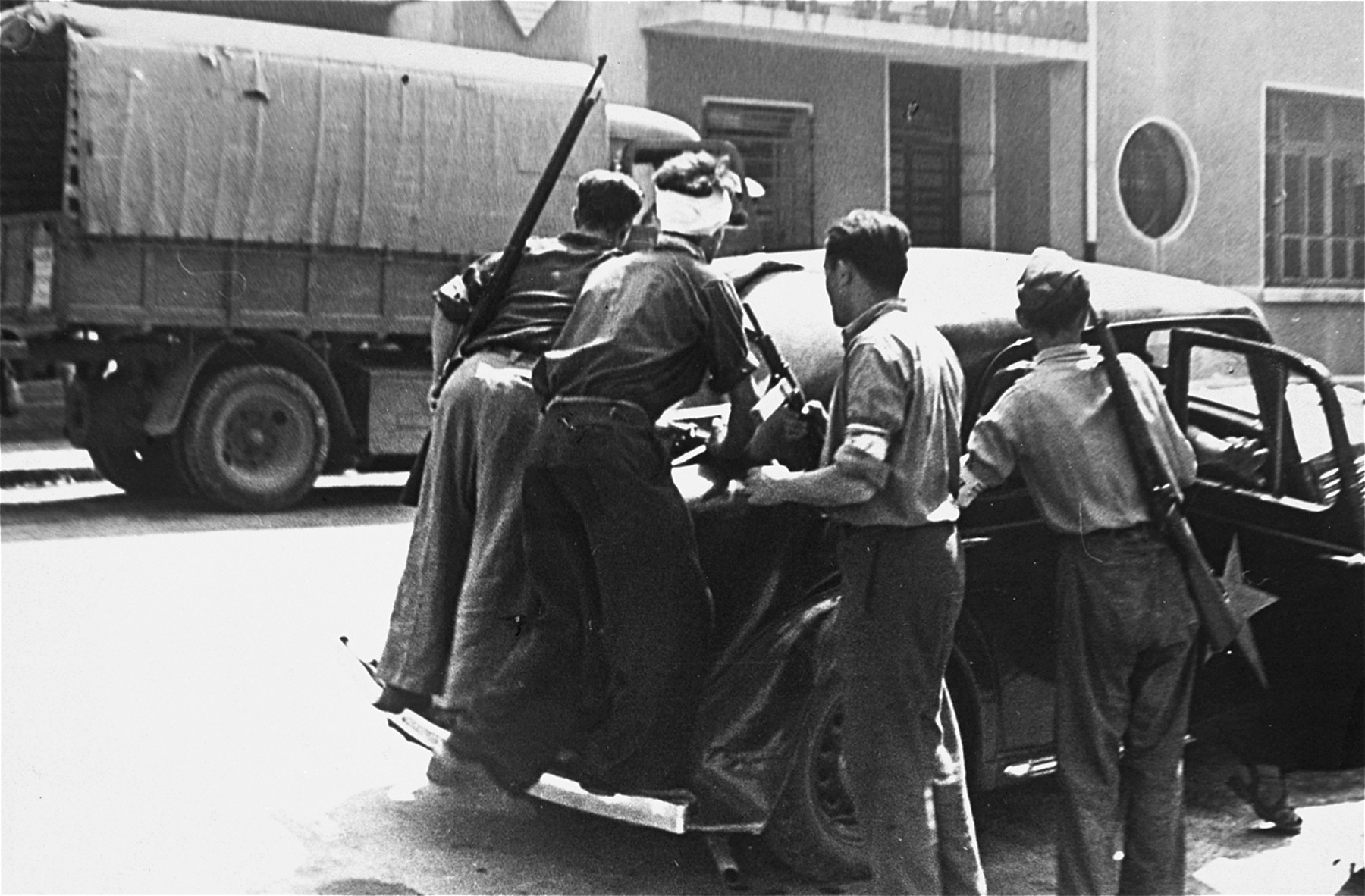 French resistance members shield themselves behind a car in front of a Ecole de Garcons during the insurrection in Marseilles that was launched to coincide with the Allied invasion of southern France.