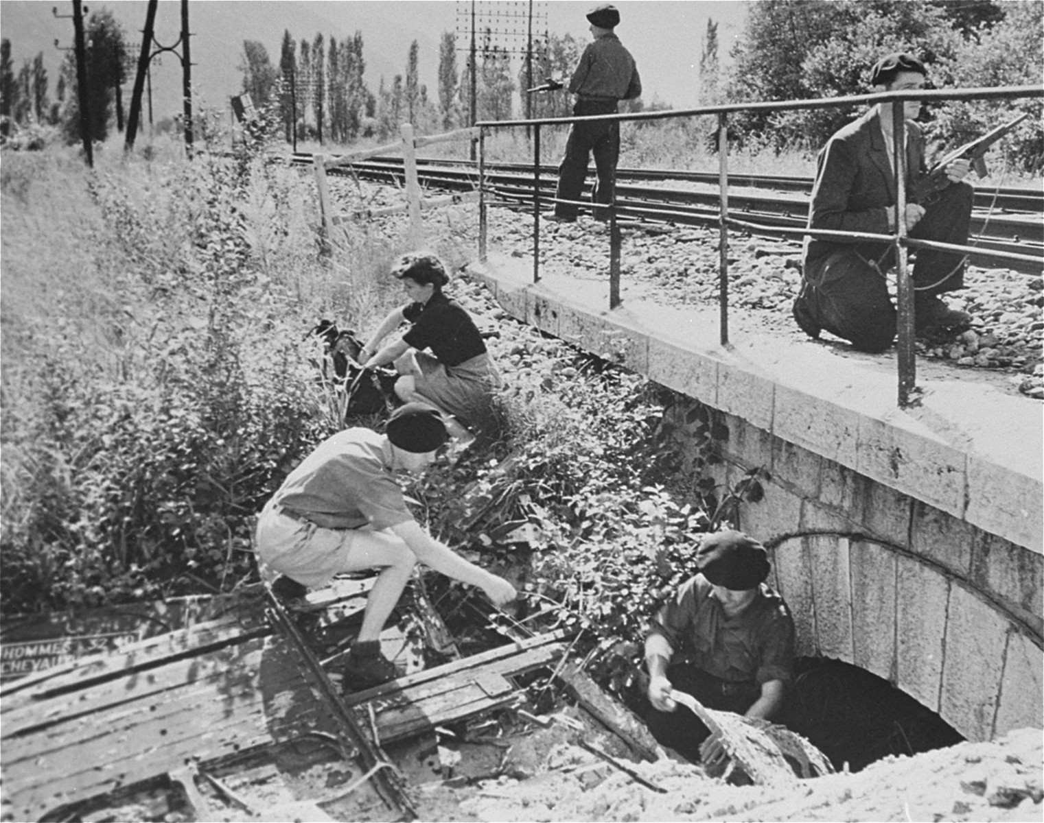 Members of the Maquis of Voireppe in the Chartreuse Region of the French Alps demonstrate the method used to place dynamite demolition charges under a railroad trestle to delay Nazi supplies.