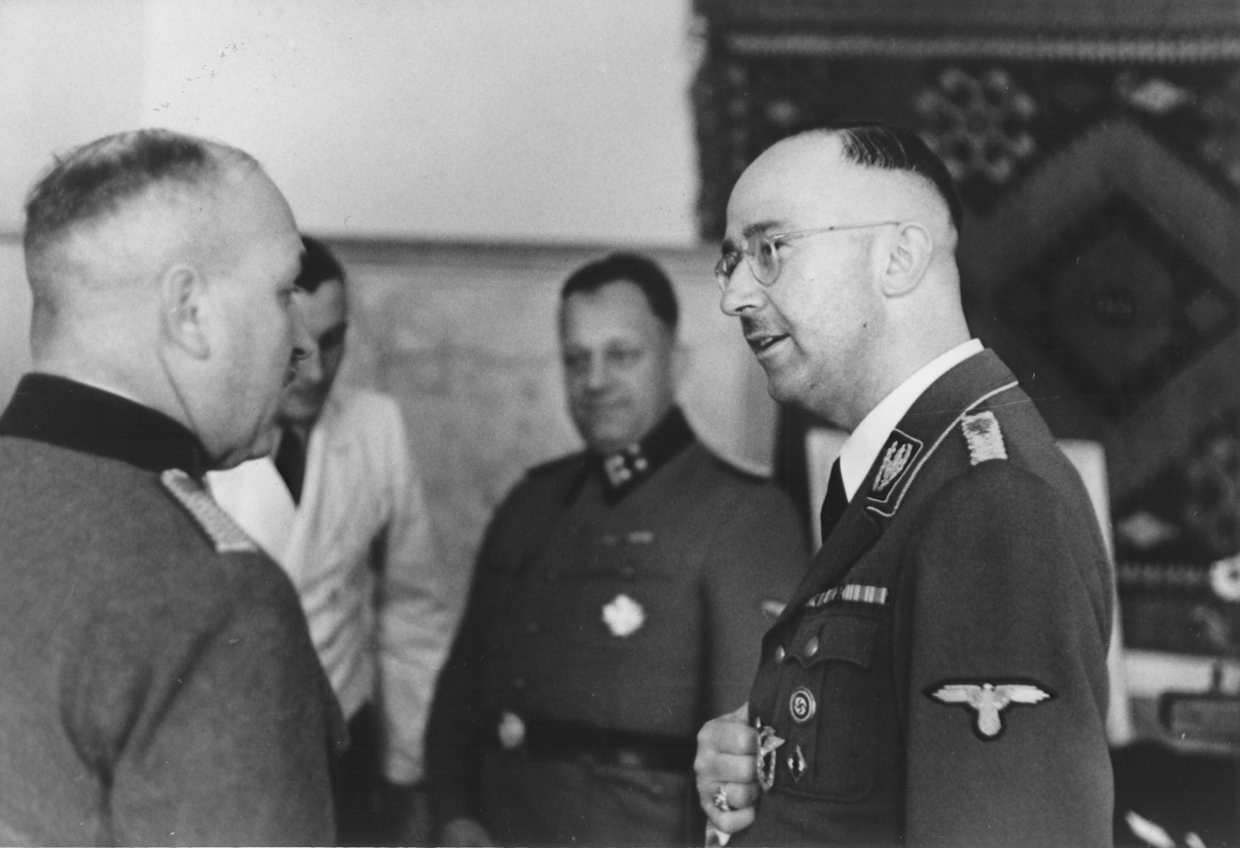Reichsfuehrer-SS Heinrich Himmler accepts the well wishes of SS police officers on the occasion of his birthday at SS headquarters in the Hegewald bei Zhitomir compound.

The man speaking with Himmler is a member of the Ordnungspolizei.  Pictured in the center SS Obersturmbannfuehrer Josef Tiefenbacher.