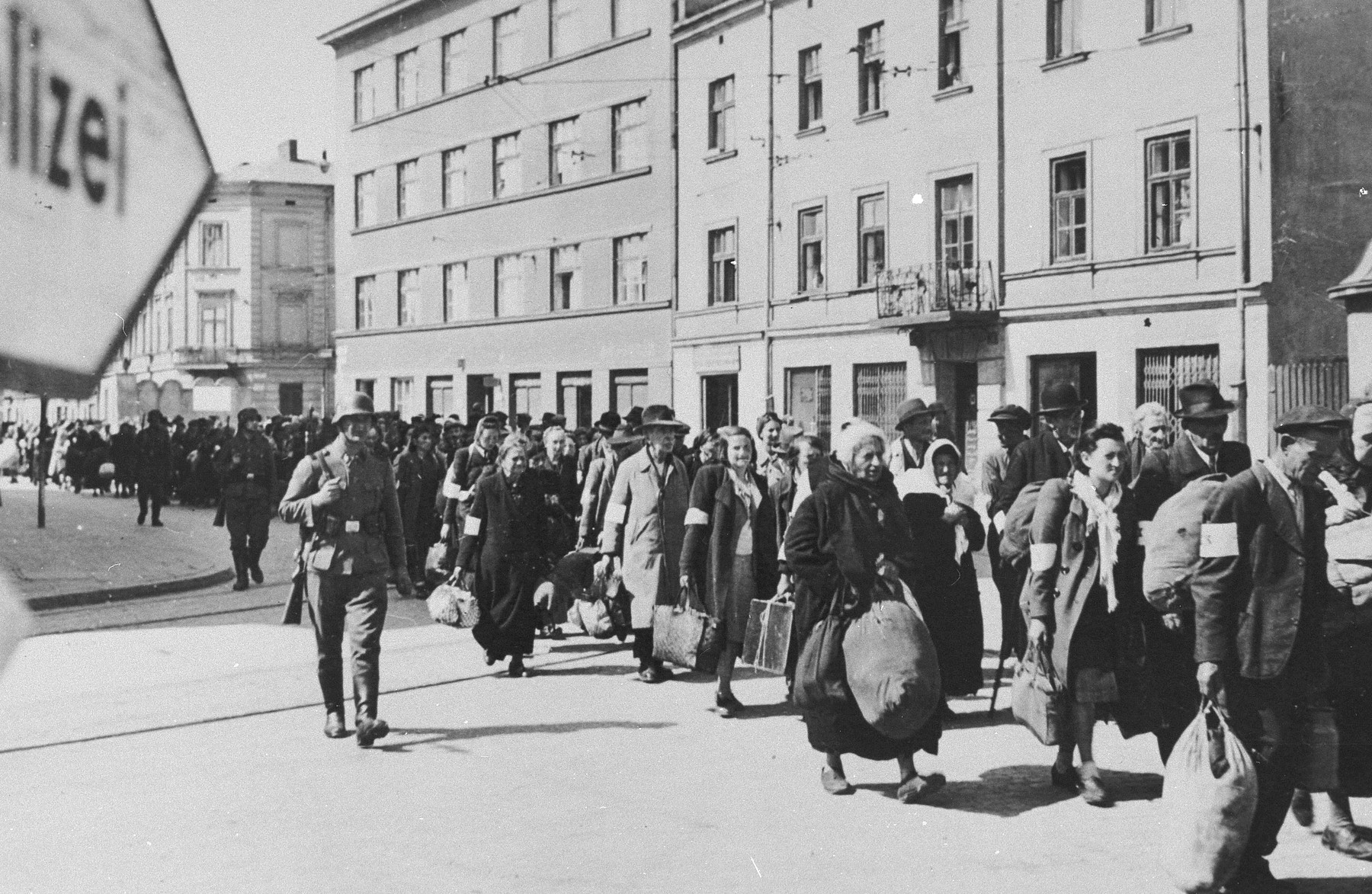 A column of Jews march with bundles down a main street in Krakow during the liquidation of the ghetto.  SS guards oversee the deportation action.