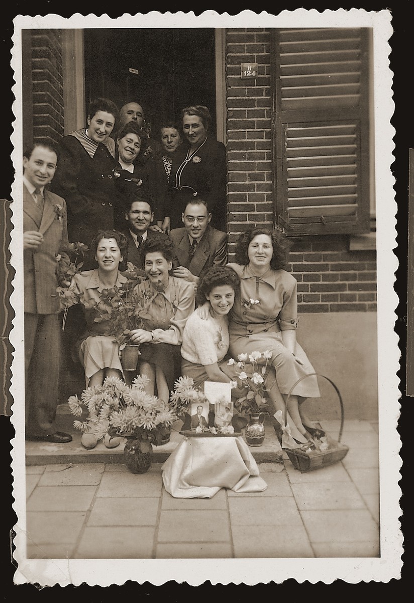 Bep Meijer (top left) with family and friends at the entrance to her family's home in Boekelo.  The photo was taken on the occasion of her sister's wedding in New York, which the family could not attend.  Pictures of the bride and groom appear in the foreground surrounded by flowers.  Bep's husband, Sallie Zion, is seated in the center below her.