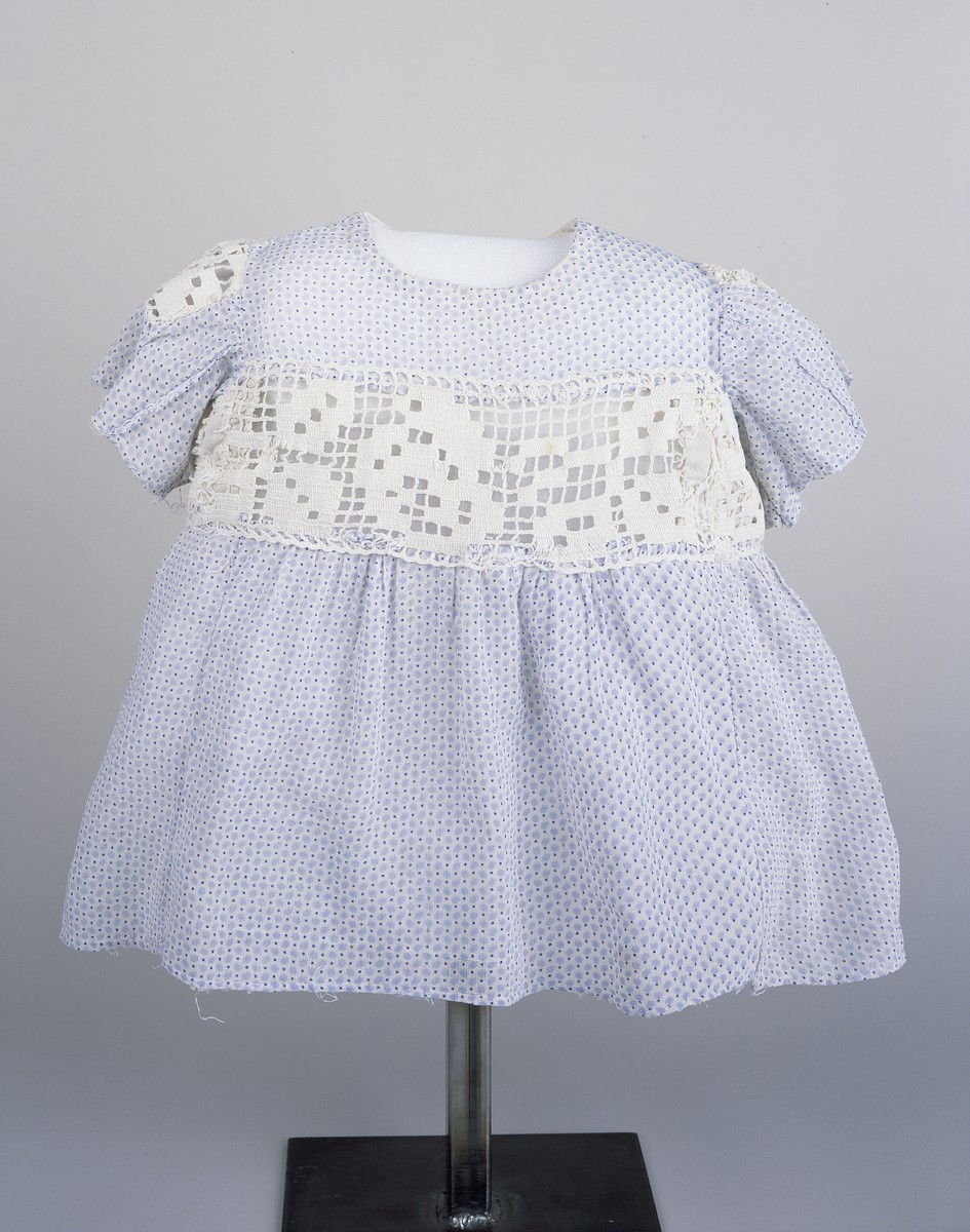 A blue and white child's dress worn by Sabina Kagan while living in hiding with the Roztropowicz family in Radziwillow, Poland during World War II.  

The dress was made by her rescuers from a doll clothing.