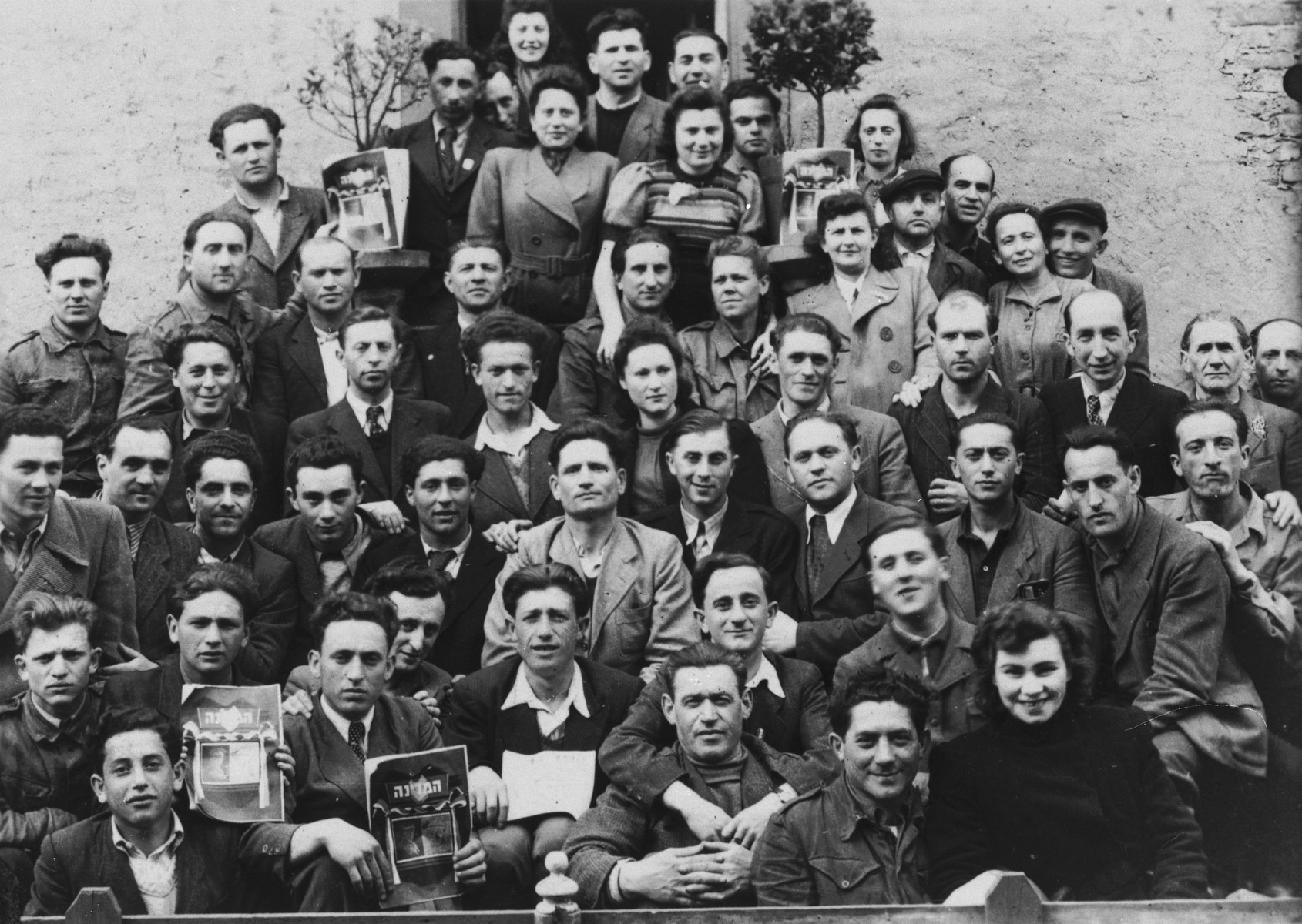 Group portrait of Jewish DPs in the Lampertheim displaced persons camp, some of whom are holding magazines.

Among those pictured is Izak Lachter (front row, second from the left, holding a dark covered periodical).  In one of the middle rows on the far right, wearing a hat is Chaim Kuperstock.  To his right is his wife, Esther (nee Lang) Kuperstock.  Pictured in the back row, middle, is Mosze Najman.  His wife, Perla Najman, is standing in front of him, to the left.
