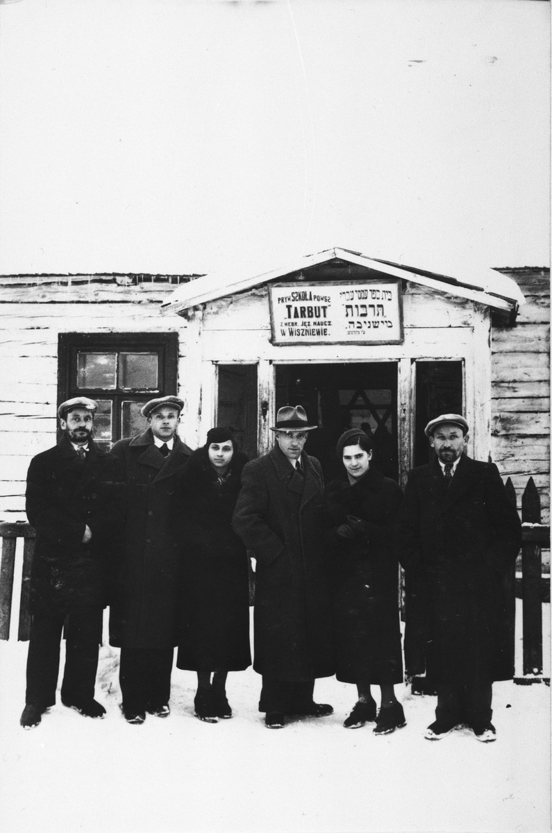 Six teachers from the Hebrew language Tarbut elementary school in Wiszniew pose outside in the snow in front of their school building.  

Among those pictured is Ralph Denishevsky (third from the right).