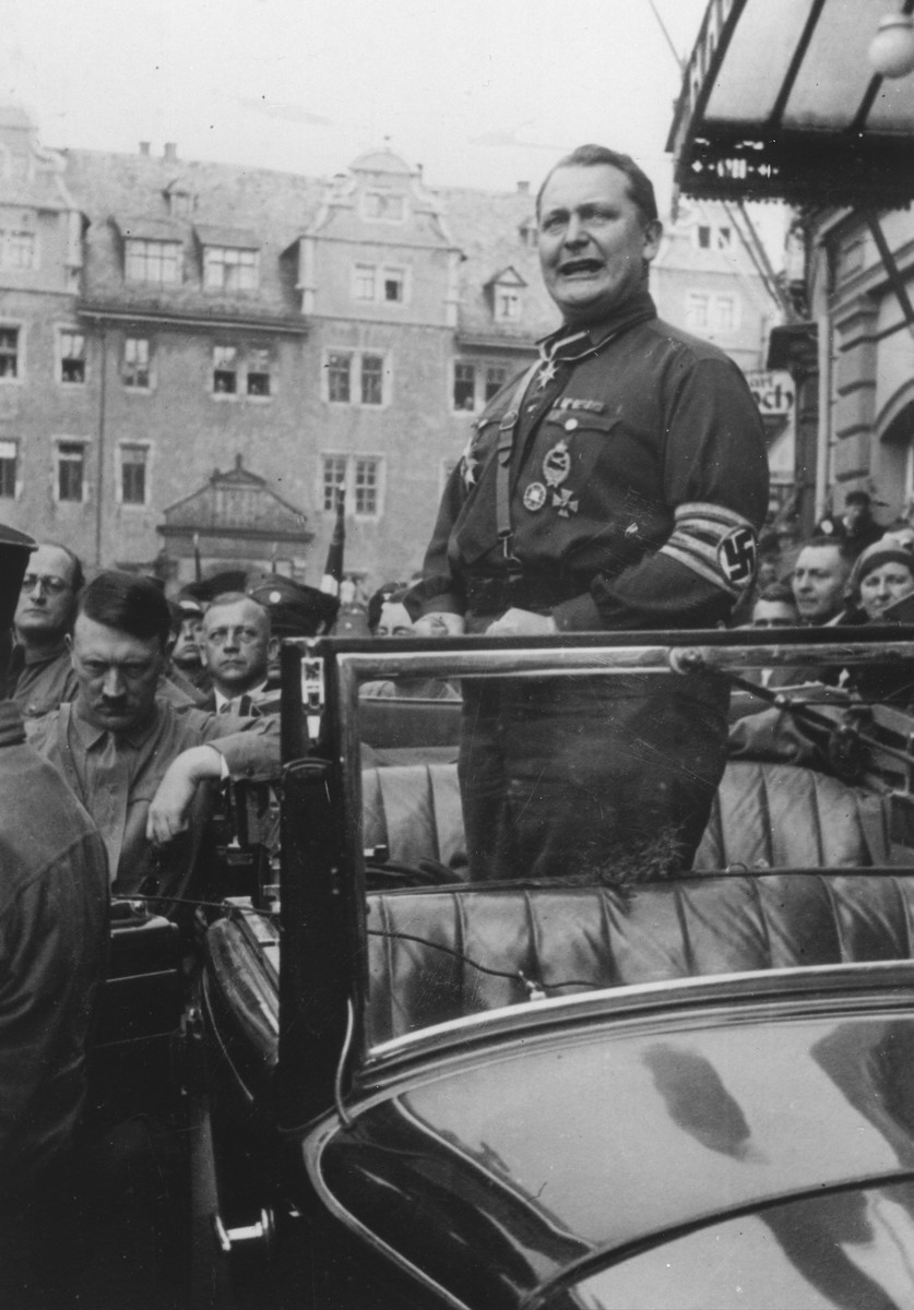 Hermann Goering delivers a speech while standing in an open car at the Gau Parteitag [District Party Day] rally in Weimar.  Adolf Hitler stands outside the car.