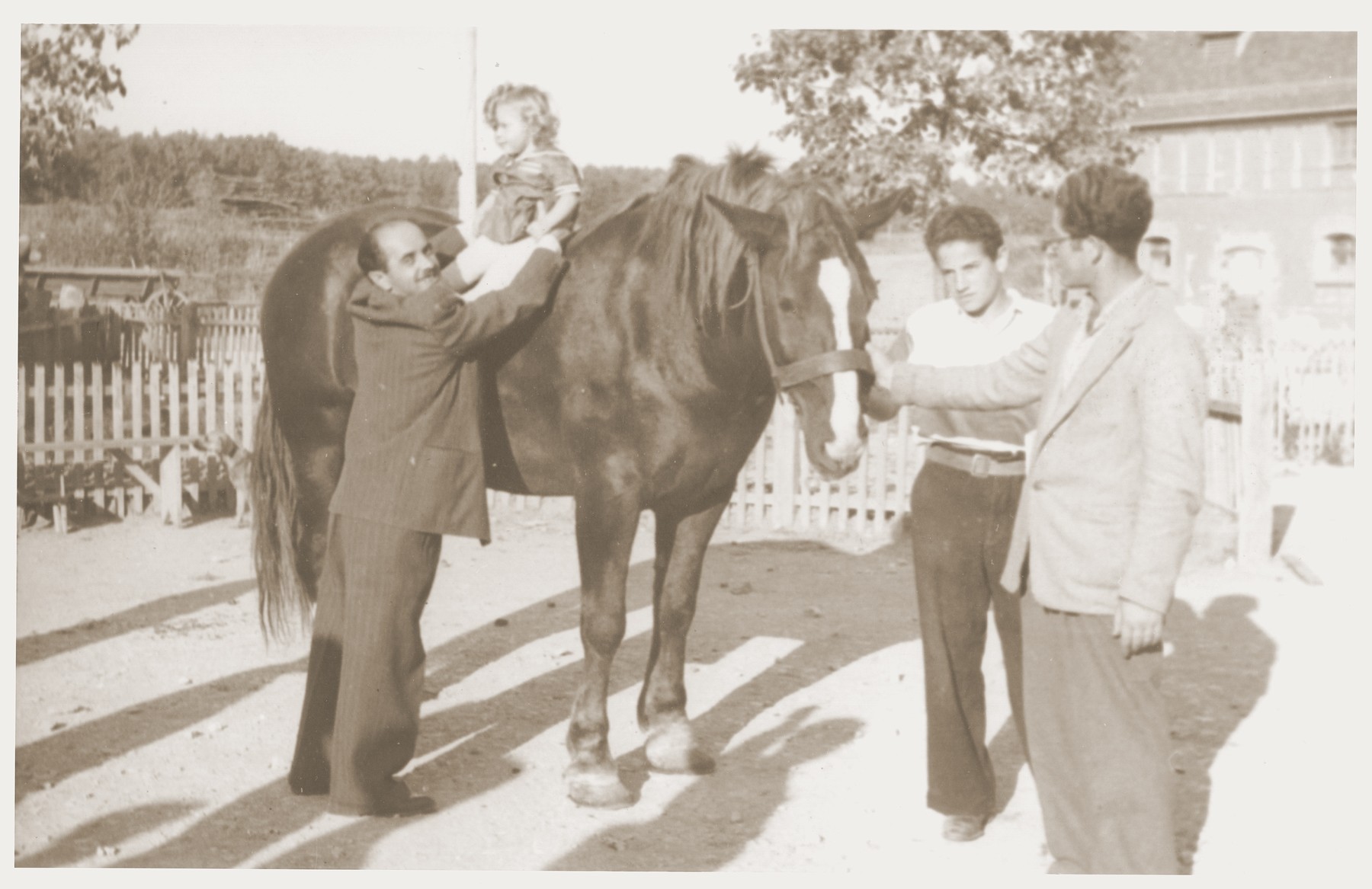 Noach Miedzinski lifts his daughter, Nili, onto one of the horses at the Kibbutz Nili hachshara (Zionist collective) in Pleikershof, Germany.