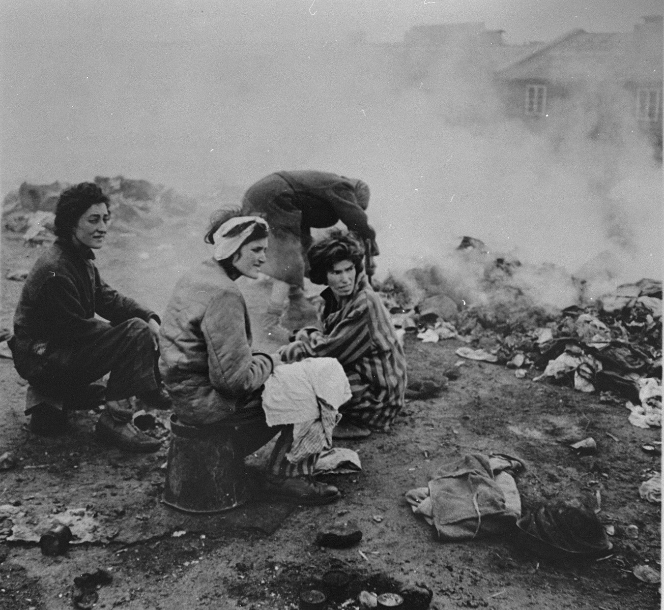 Survivors in Bergen-Belsen sit amongst clothing that is  being burned to control an outbreak of typhus.