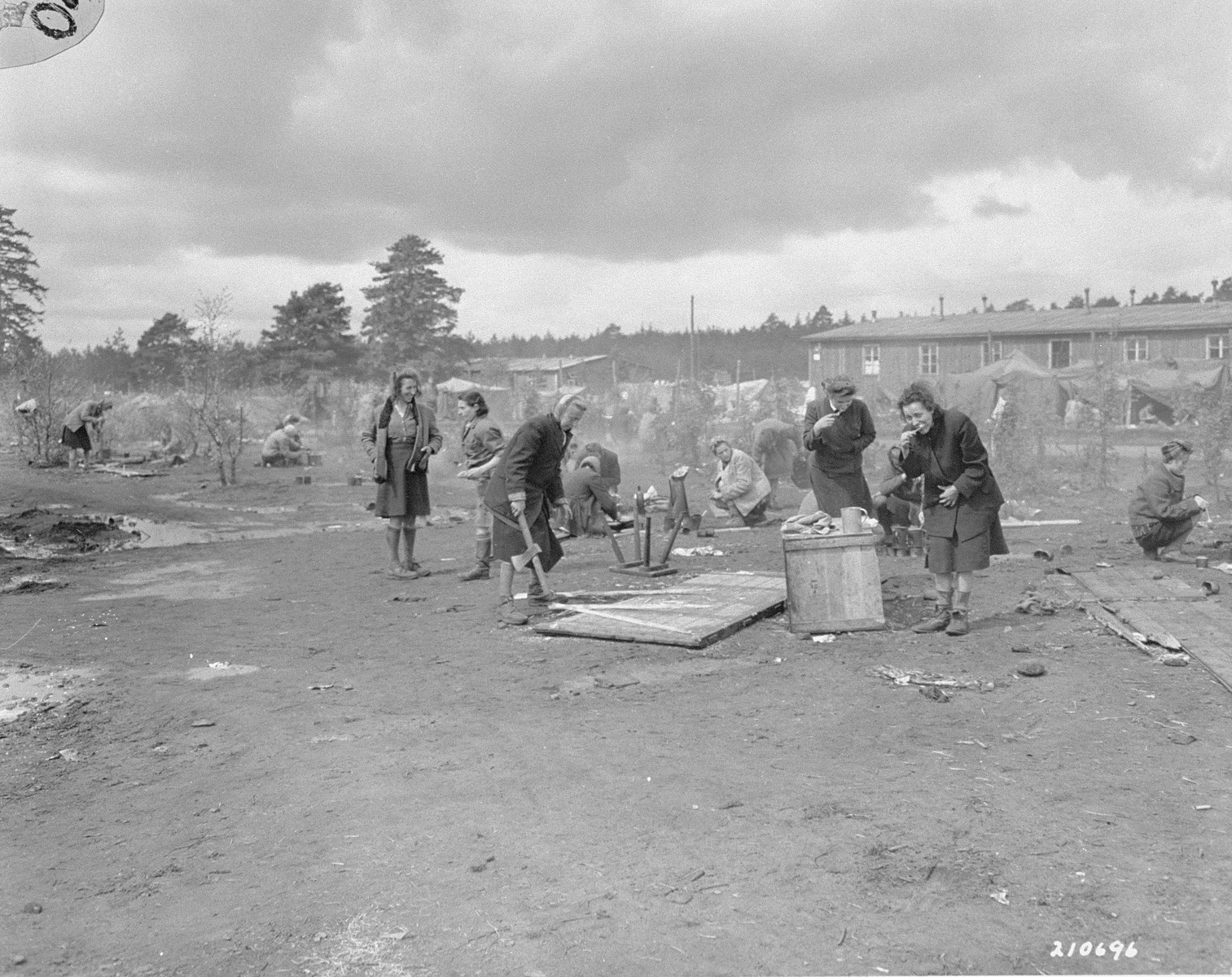 Survivors in Bergen-Belsen tend to chores after their liberation.

The original caption reads: "Women political prisoners, freed by advancing allied armies at their German prison camp at Belson [sic], Germany, wash their teeth with utensils supplied them by their liberators.  Woman at left is chopping up a door for fire wood.  Camp is now operated by British 2nd Army."