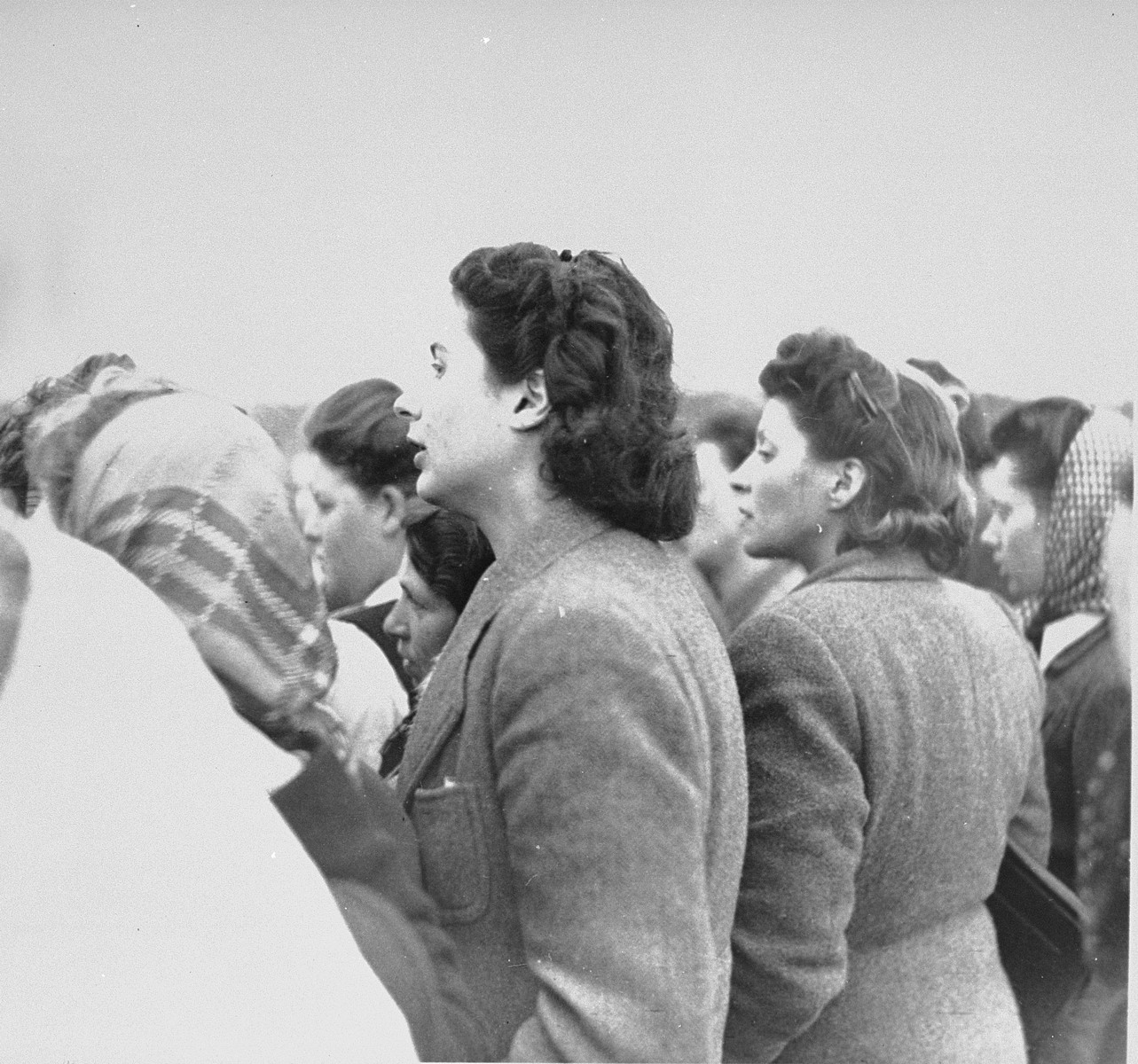 Women survivors in Bergen-Belsen watch British troops forcing former SS guards to bury corpses in a mass grave.