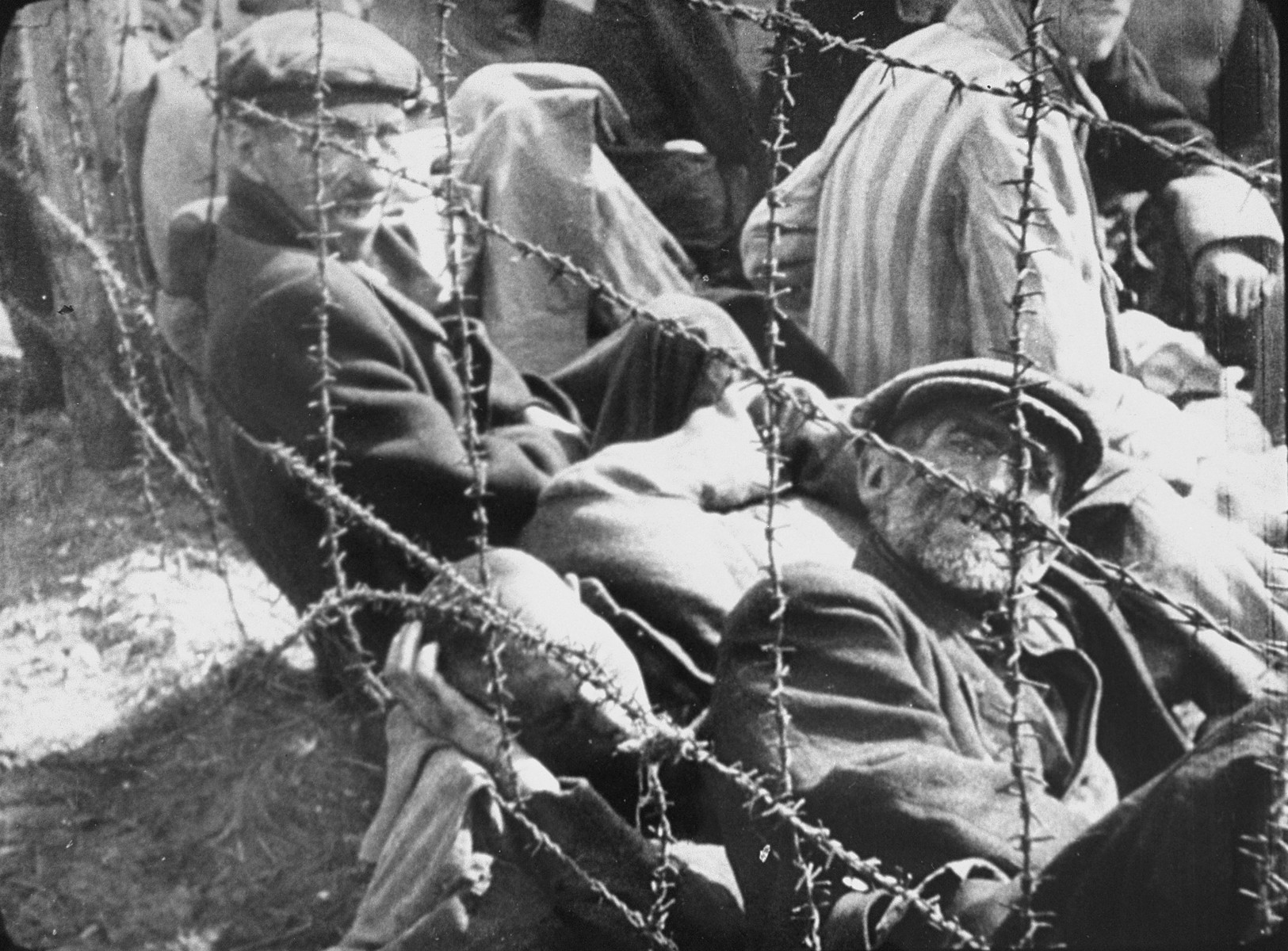 Survivors in Bergen-Belsen concentration camp rest behind a barbed wire fence after liberation.