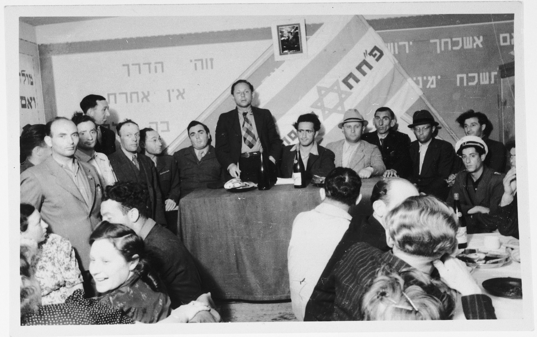 Members of the Zionist group Partizanim-Hayyalim-Halutzim meet in the Zeilsheim displaced persons' camp held in a room decorated with a flag and posters.
