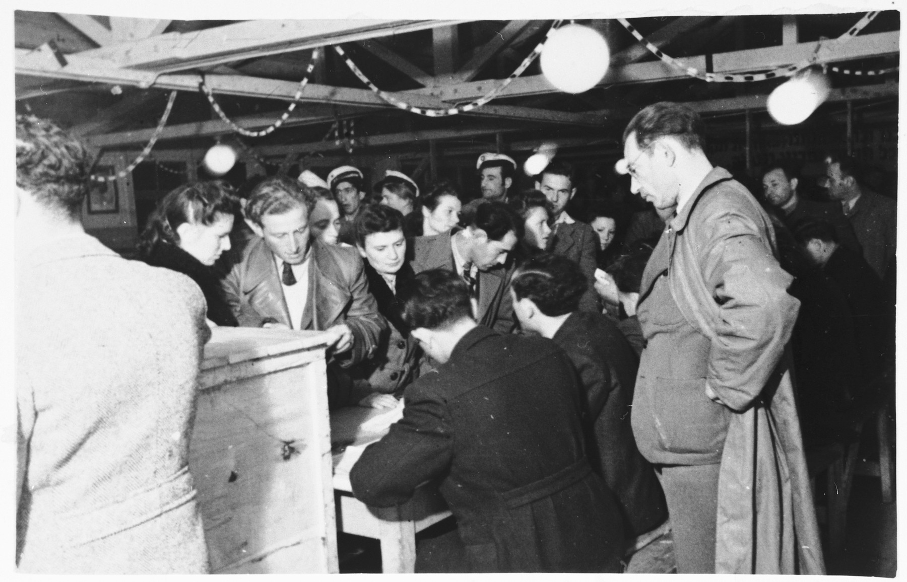 Men and women file past a table to vote in elections in the Zeilsheim displaced persons' camp.

Among those pictured is Abraham Poznanski, in the center of the photo, looking down at the table, in profile.  His wife, Hanka (Anna) Poznanski is standing behind him, looking off to the right.