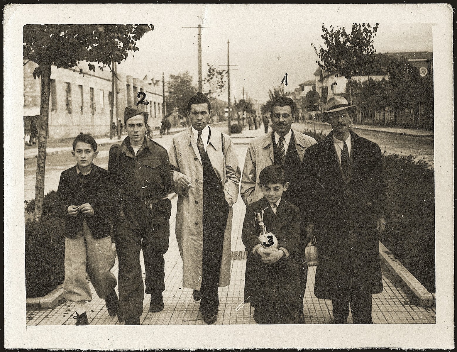 Mosa (Moshe) Mandil, Gavra, and Refik Veseli walk along the streets of Tirana with friends on liberation day.  In 1990 Refik Veseli was recognized by Yad Vashem as one of the Righteous Among the Nations.

Mosa is pictured second from the right, Gavra walks ahead of him, Michael Komforti is on the far left and Refik is second from the left.