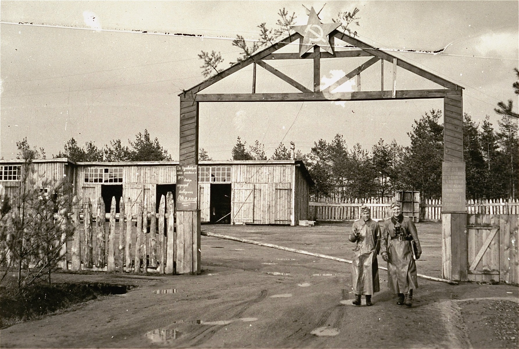 Two German soldiers stand outside of the gate of an abandoned Soviet camp.