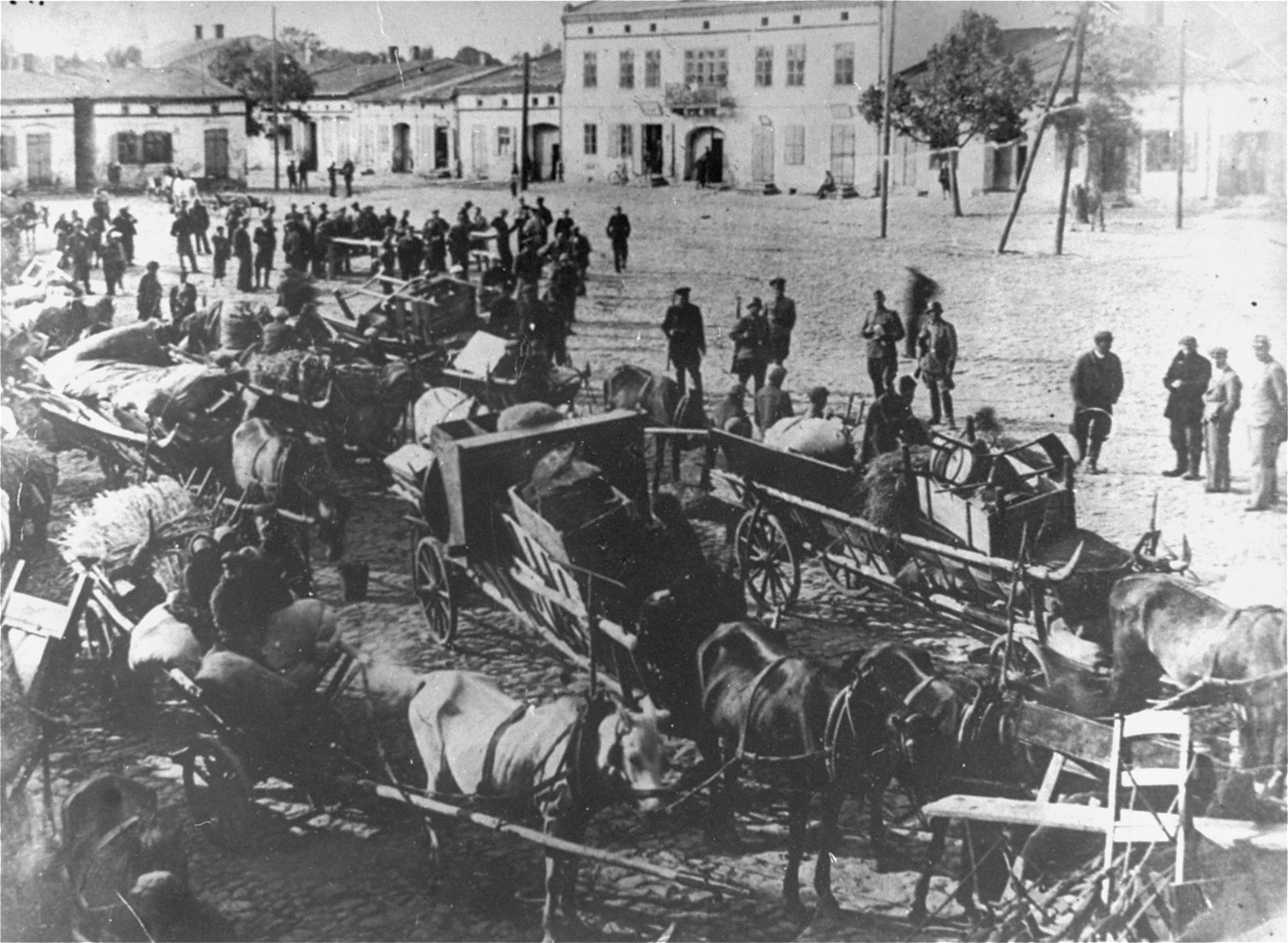 German troops stand in the town sqaure of Przyrow where dozens of horse-drawn wagons are gathered [presumably during a resettlement action].  [oversized print]