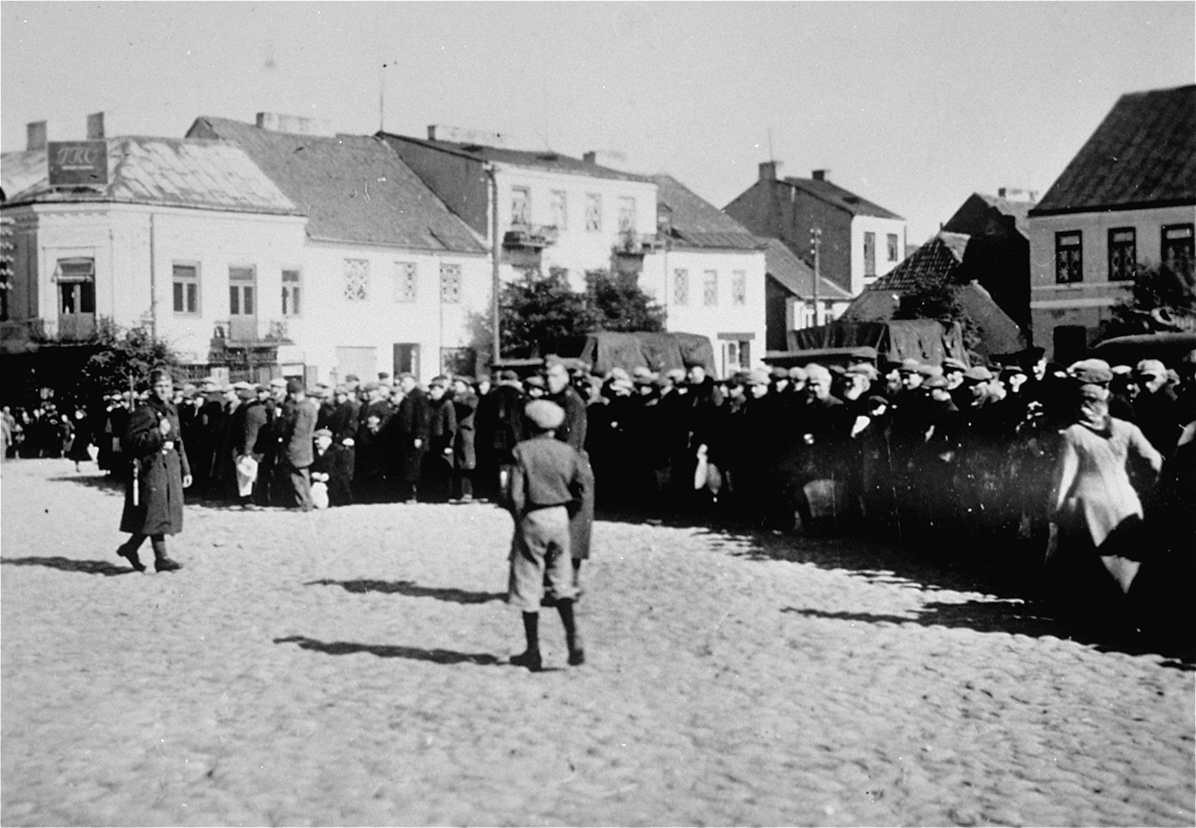 Jewish men are lined up along the perimeter of the town square in Raciaz.