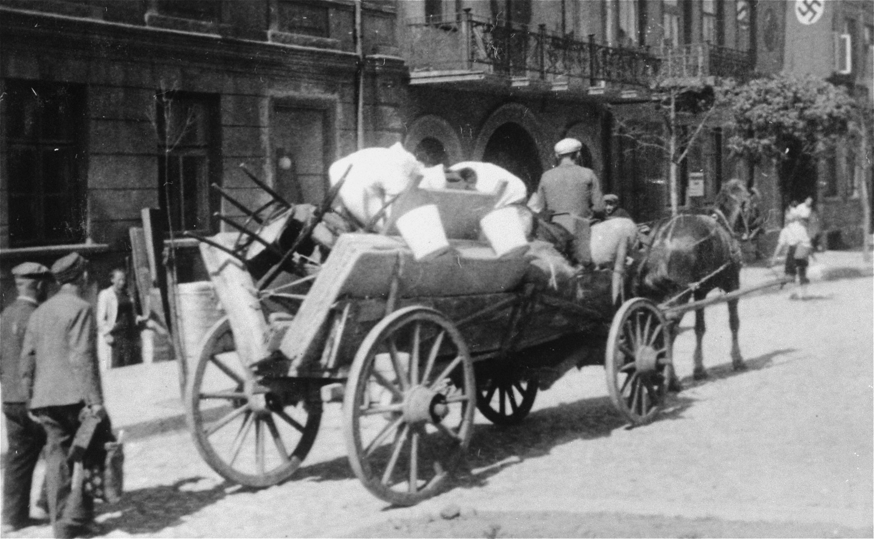 A Jew drives a horse-drawn wagon bearing furniture and household goods along a street in Plonsk.

The original German caption reads: "Juden raus!"