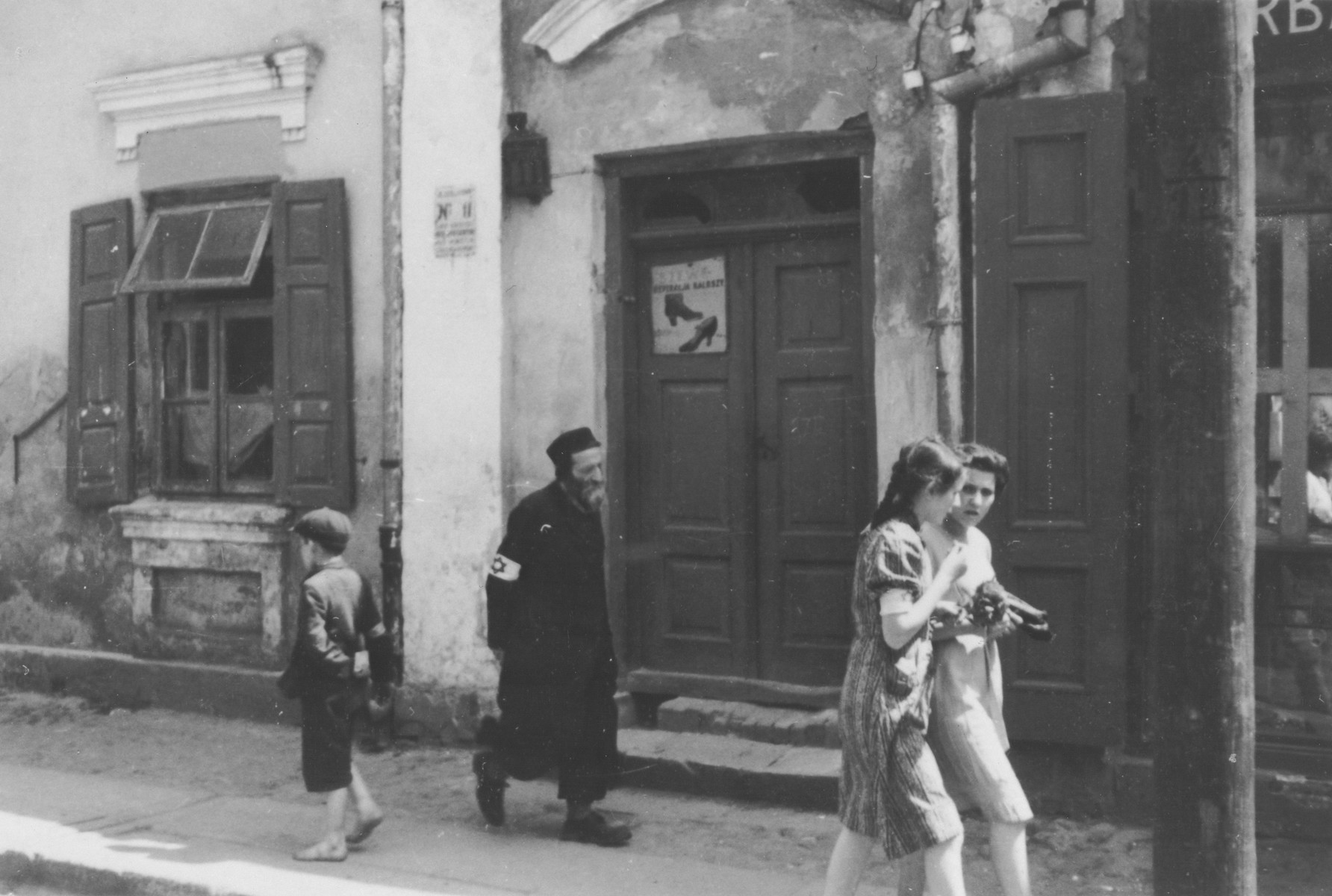 Polish Jews wearing armbands walk down a commercial street in an unidentified ghetto.