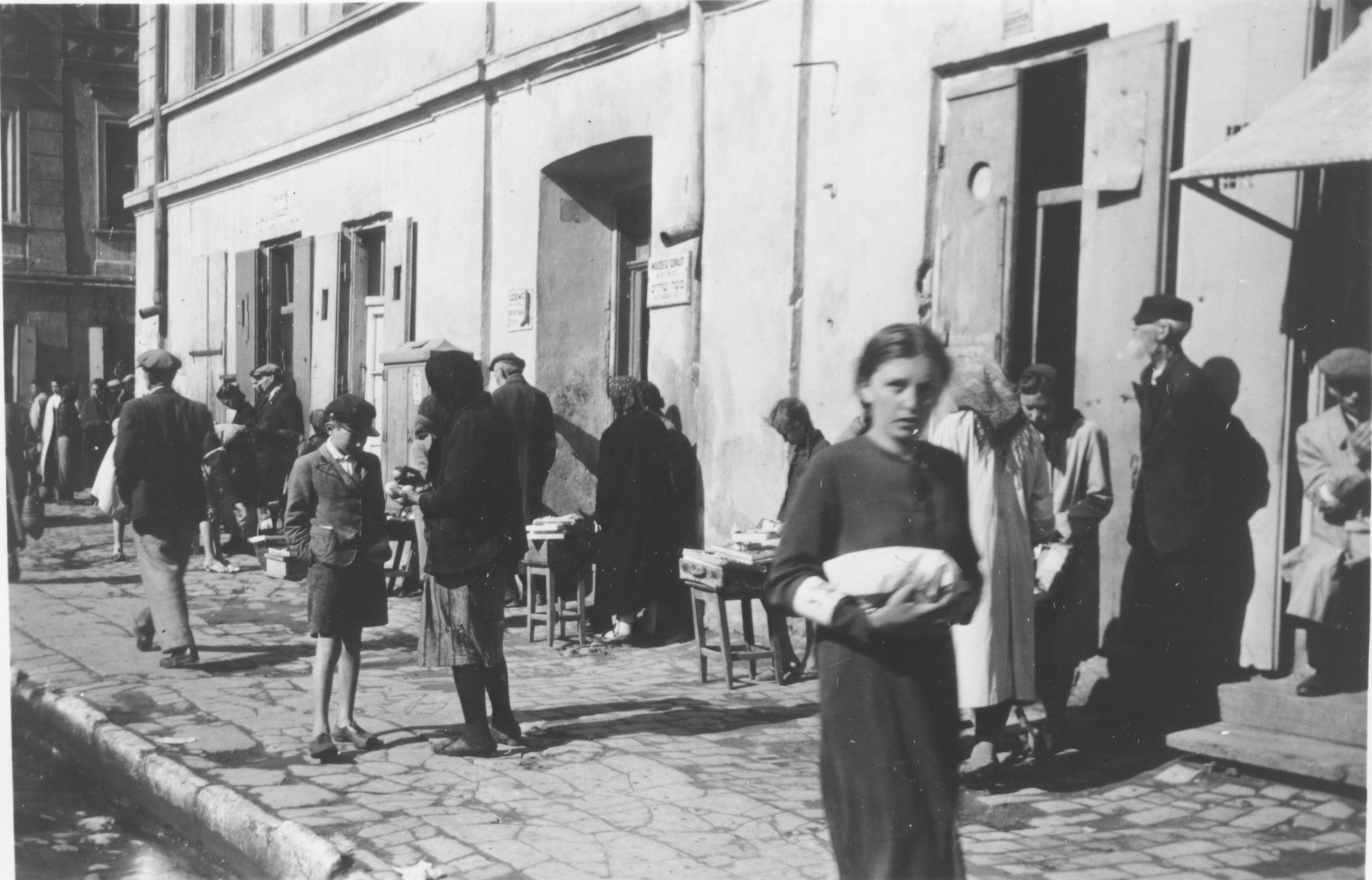 Polish Jews wearing armbands walk down a commercial street in an unidentified ghetto.