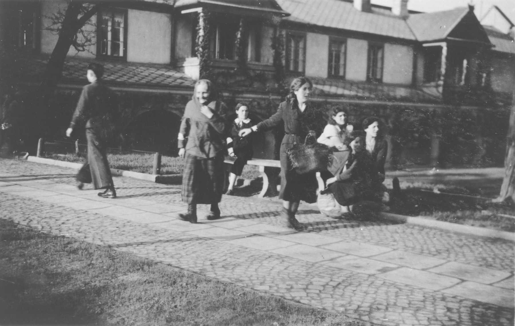 Men and women walk down a street and sit on benches in an unidentified ghetto.