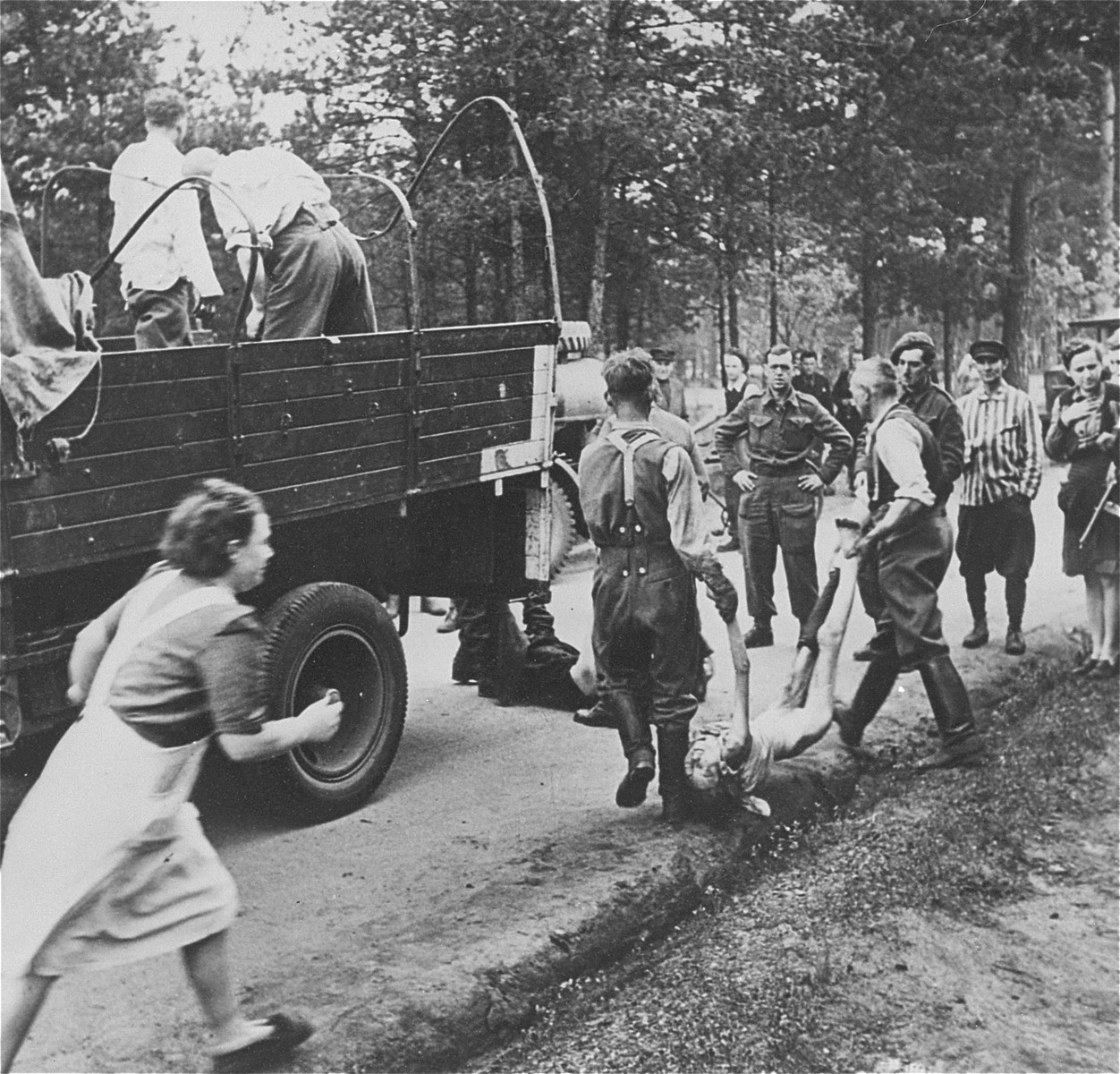 Under British guard, former SS guards in Bergen-Belsen are forced to load the corpses of prisoners onto trucks, for transport to mass graves.

Running after the truck is Clara Spiegler (later Silbernik), who became furious after seeing SS throw the corpse of her best friend onto the truck.