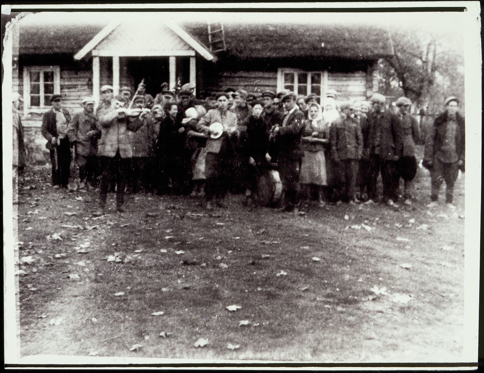 Peasants, some with musical instruments, celebrate the redistribution of land in the region.  

Luba Ginunski, one of the shtetl's leading Communists, distributed land to five hundred poor Polish peasants in the autumn of 1940.  Luba, is pictured dressed in black, speaking to a woman with a white kerchief.  She survived the war in the Soviet interior and afterwards immigrated to Israel.