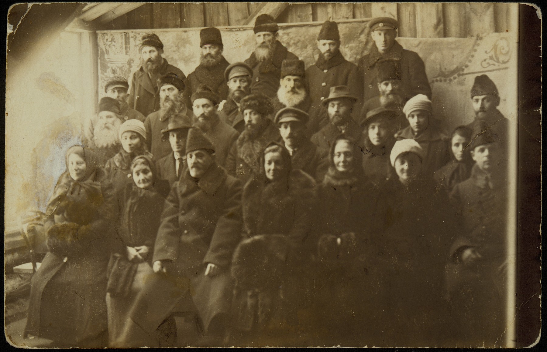 Group portrait of the Assistance Committee responsible for distributing donations of money to Eisiskes from America. 

The photo was taken in honor of Aaron-Don Becker (front row, third from left), who in 1920 brought a large donation to the shtetl from the Eishyshker Society in New York.  Seated to the right of Aaron-Don is his relative Sarah Kaganowicz, to his left is Hayya Sonenson, head of the Froyen Farain (Union of Women); Libe-Gittel Rudzin; her daughter, Miriam Kaganowicz; and husband Shael, relatives of Aaron-Dan.  Also pictured in the photo are members of the Pachianko family, members of the Kahal, and clergy.  Standing in the back, between Aaron-Don and Hayya Sonenson, is Reb Hertz Mendl Hutner, the shtetl judge.