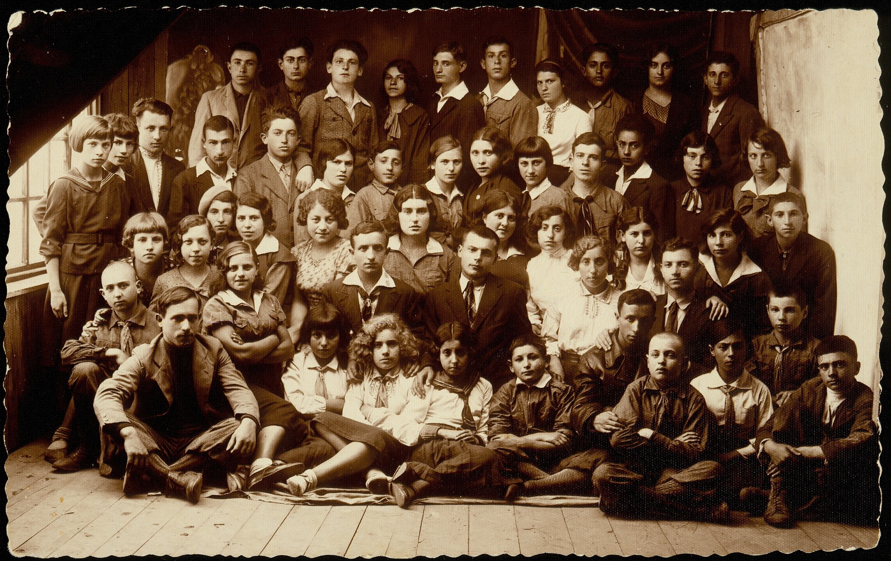 A special meeting of Hashomer Hatzair in Eisiskes attended by counselors from Vilna, including Abba Kovner.  

Among those pictured are: top row, from right to left: Boyarski, Krupski, Kaplan, Bichvid, unknown, son of Aronka, Reb Yoshe the coachman's son, unknown;  second rowfrom the top:  Michalowski, Boyarski, Krupski, Bichvid, Cofnas, Portnoy, Borshanski, Levitan (first names are unknown); third row from the top: Herzl, Miriam Lewinson, Lebovitz, Ginunski; fourth row from the top: Garmenishki, Rosenblum, Shalom Kahn, Reuven Paikowski.  Sitting on the floor are Abba Kovner (with his hand on the boy in front of him), Manosh Blacharowicz, and Stoller (the girl in the center with blond curly hair).  

Only 11 of those pictured survived the Holocaust, among them Abba Kovner and Reuven Paikowski.