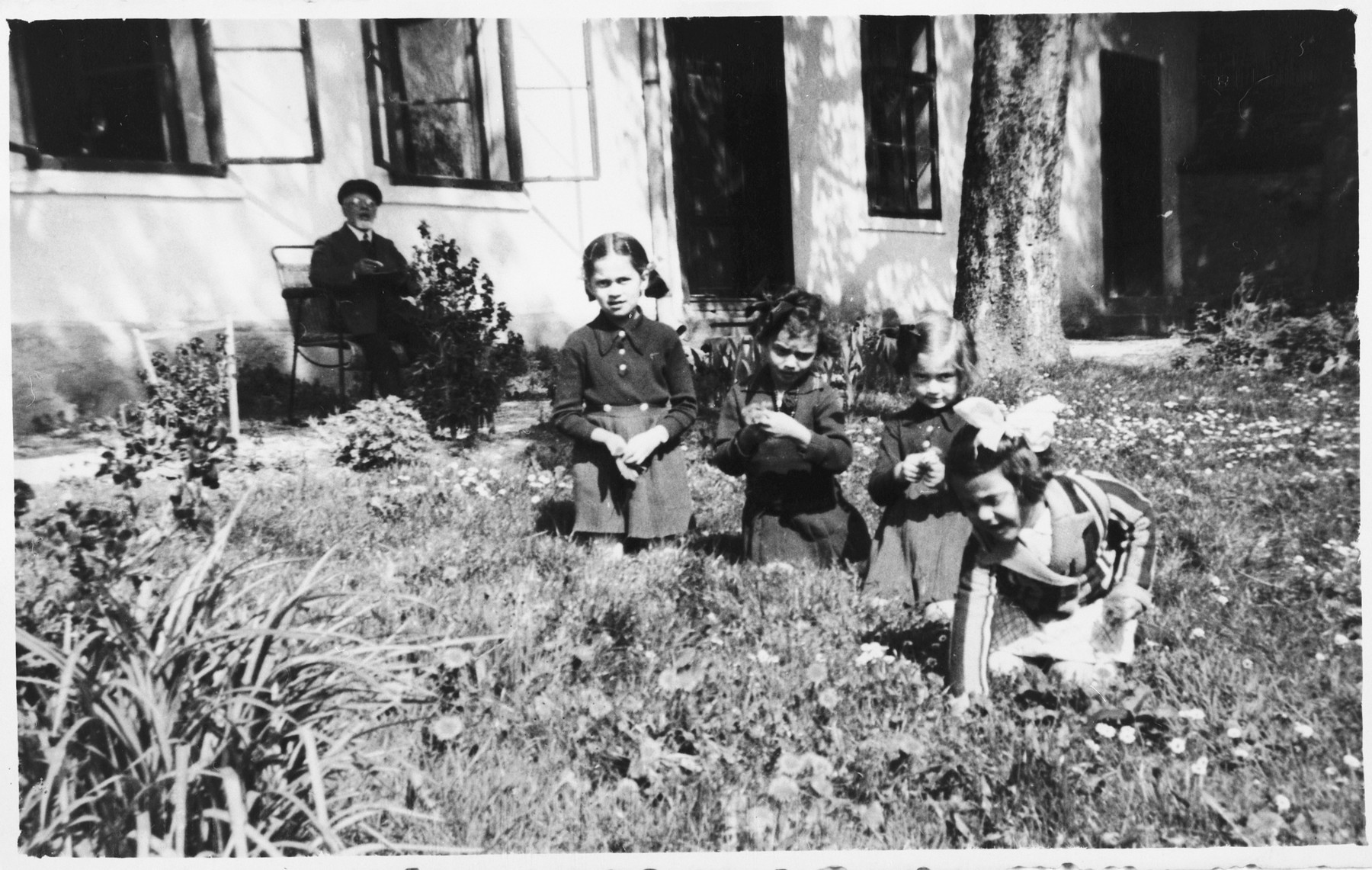 Four young Jewish girls play in the garden while their grandfather looks on.

Pictured are Zdenka and Vera Apler and Edita Deutsch.  In the background is Rabbi Leopold Deutsch.  He is seated in front of a building that served both as the Deutsch home and the local synagogue.