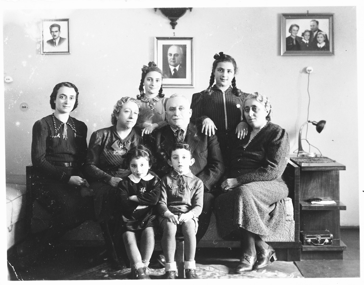 A Jewish family poses in their apartment with two young Jewish children they are taking care of, who were recently released from the Djakovo concentration camp.

Pictured are members of the Spitzer family shortly before the deportation of the Jewish community of Osijek. Standing in the back row, form left to right are Leah and Miriam Spitzer; in the middle row are Ilonka Spitzer, Riza Krasso and Mr. and Mrs. Spitzer, the parents of Marko Spitzer.  At the time of this photograph, Marko Spitzer was already in a POW camp, and Alfred Krasso was imprisoned in Jasenovac.