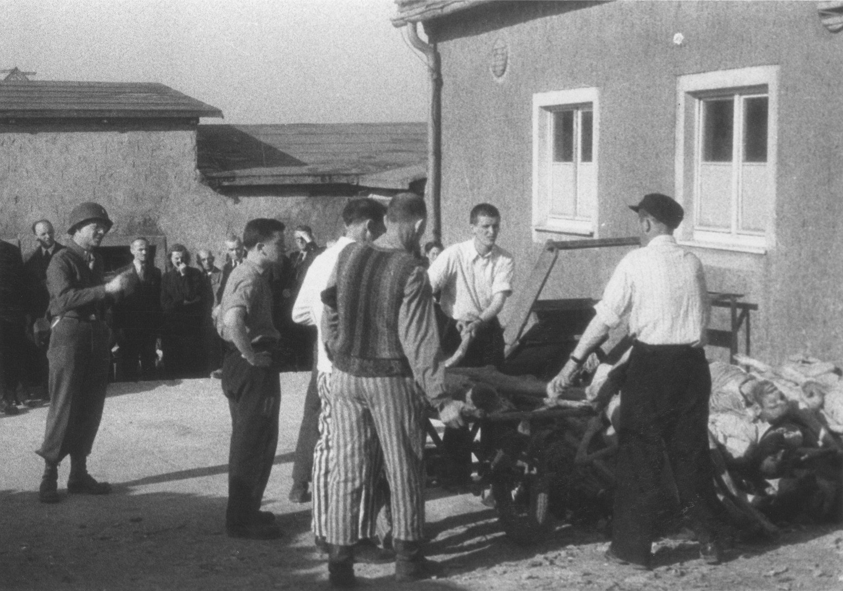 Survivors stack corpses outside the crematorium in the newly liberated Buchenwald concentration camp while German civilians look on.